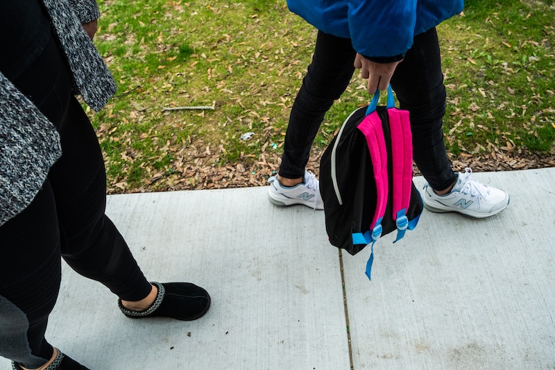 A close up view of two people walking down a sidewalk, one person is carrying a backpack.