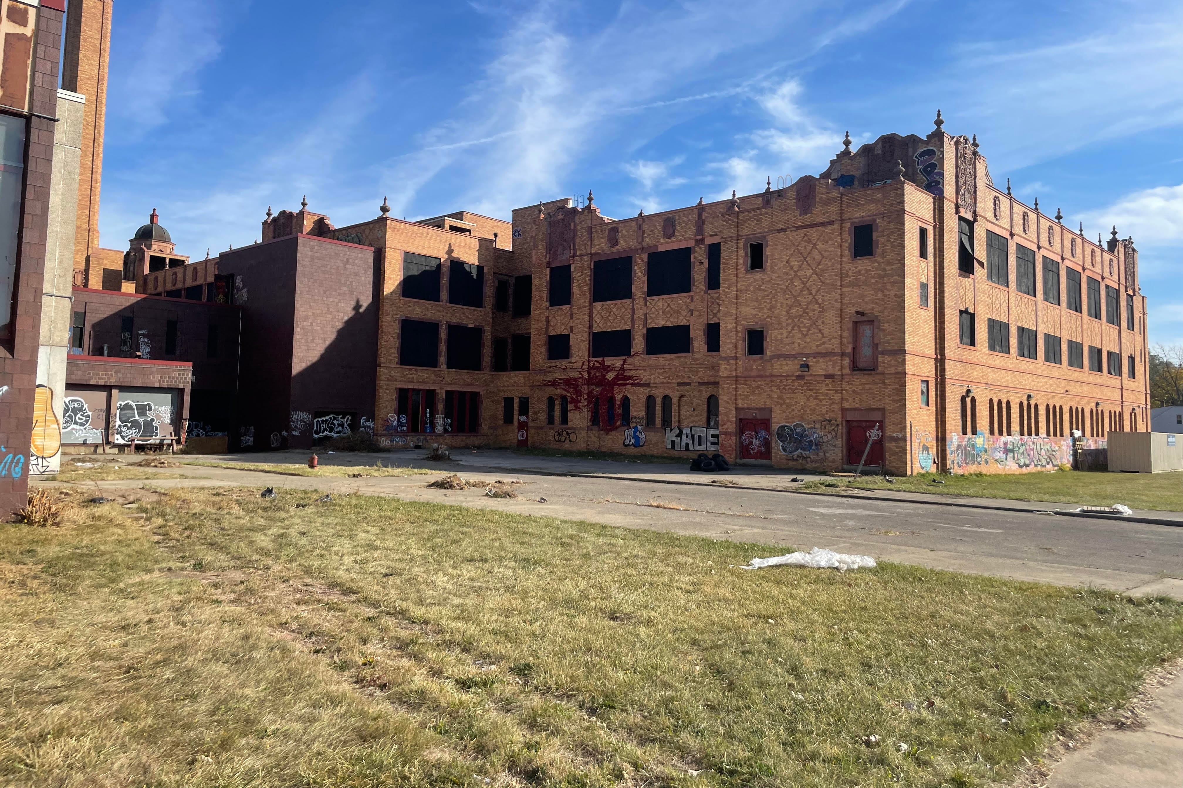 A landscape shot of a vacant high school building, with boarded and broken windows as well as graffiti tags along the facade.