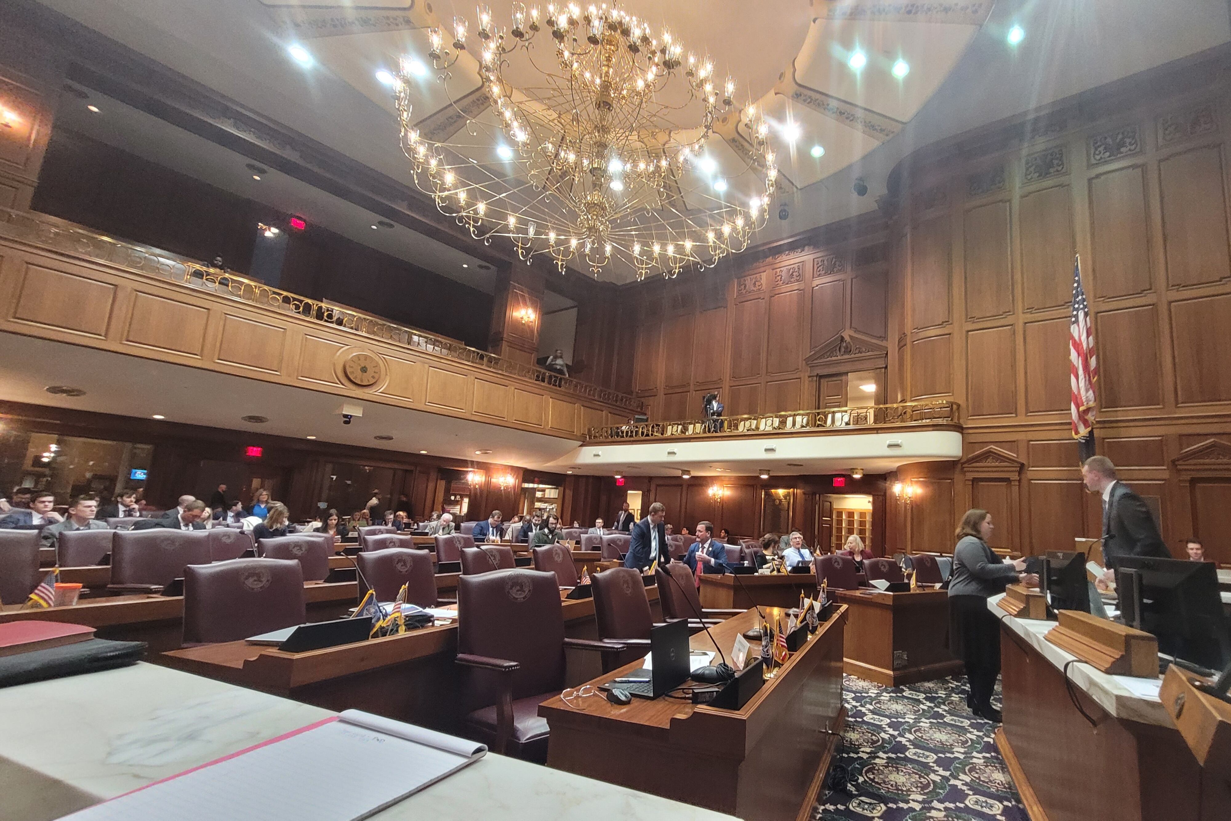 Inside the Indiana House Chamber on the day of a House Education Committee meeting, with lawmakers not yet in their seats and a chandelier overhead.