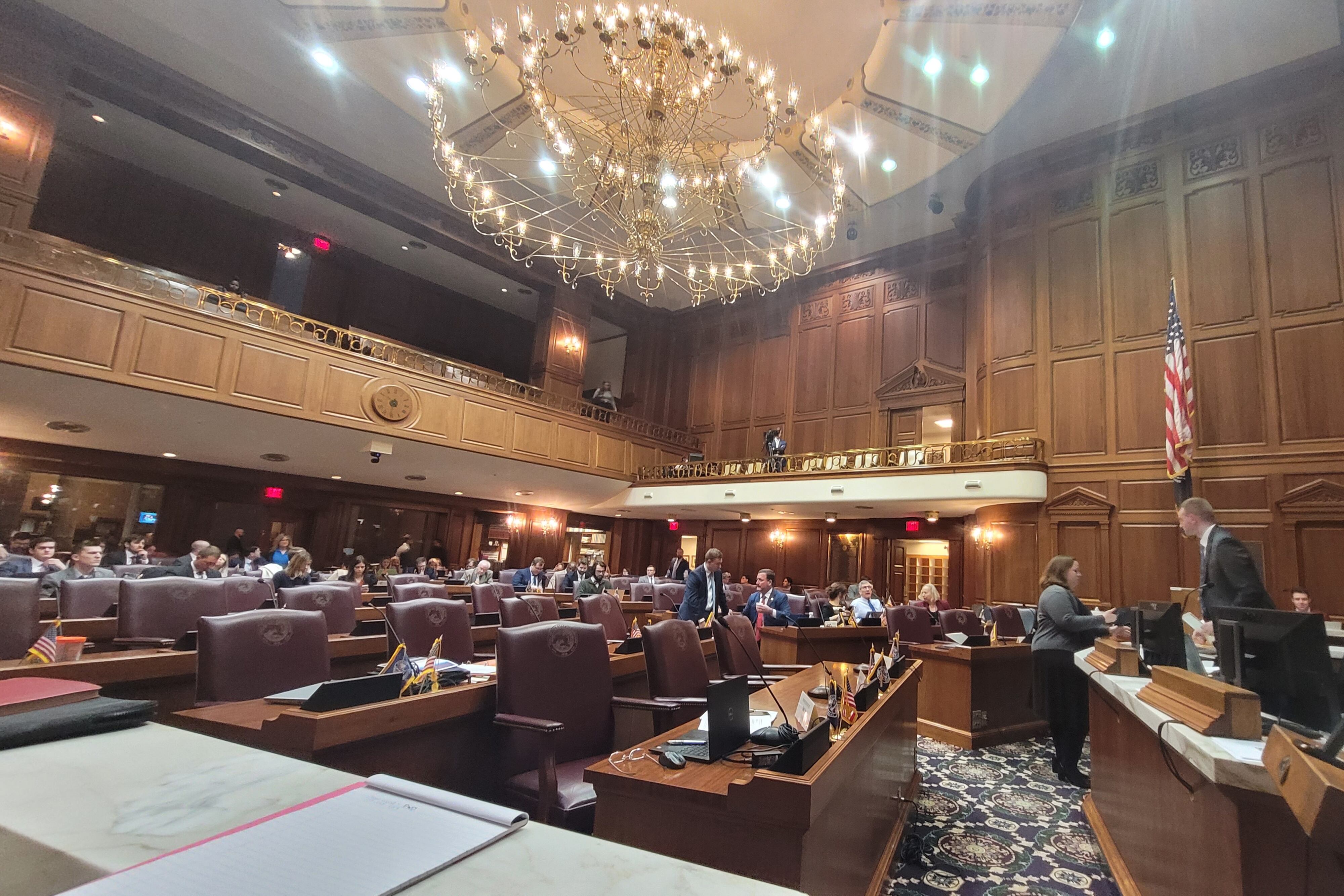 Inside the Indiana House Chamber on the day of a House Education Committee meeting, with lawmakers not yet in their seats and a chandelier overhead.