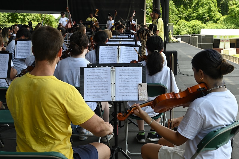 A photograph of high school students playing instruments on an outdoor stage.
