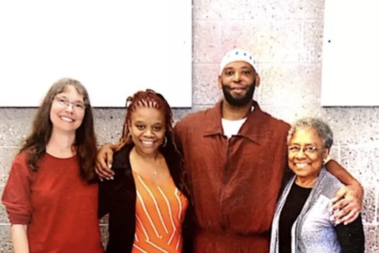 Four people, one man and three women, posing together in front of a wall.