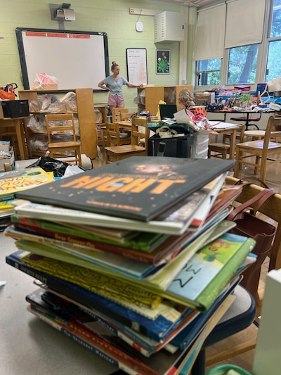 An adult woman and a young child stand in the middle of a cluttered classroom.