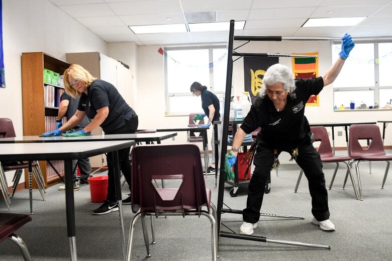Gloved workers wipe tables and panels in a classroom.