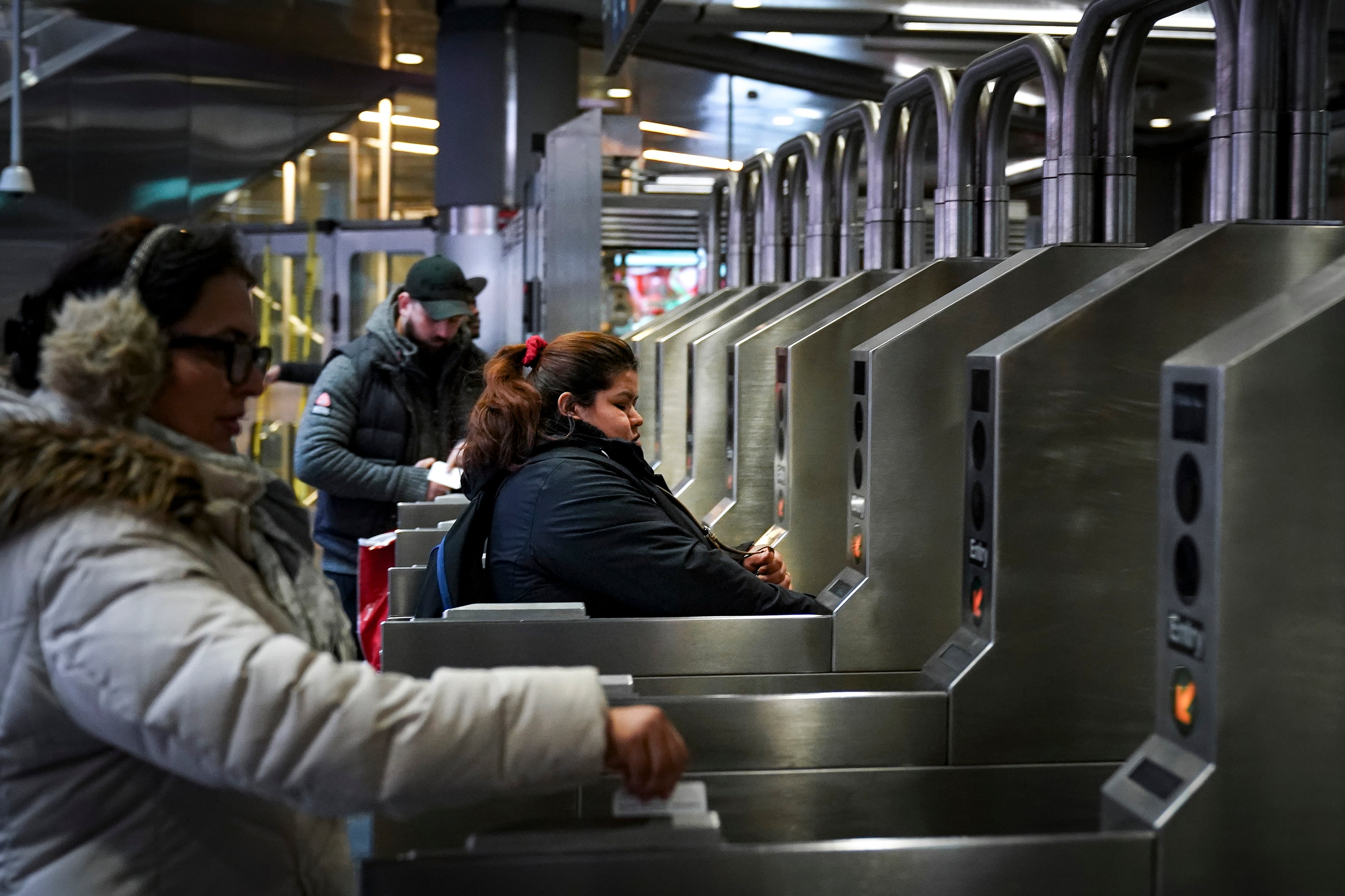 Three people wearing winter clothes swipe their metro cards to enter the New York City subway.