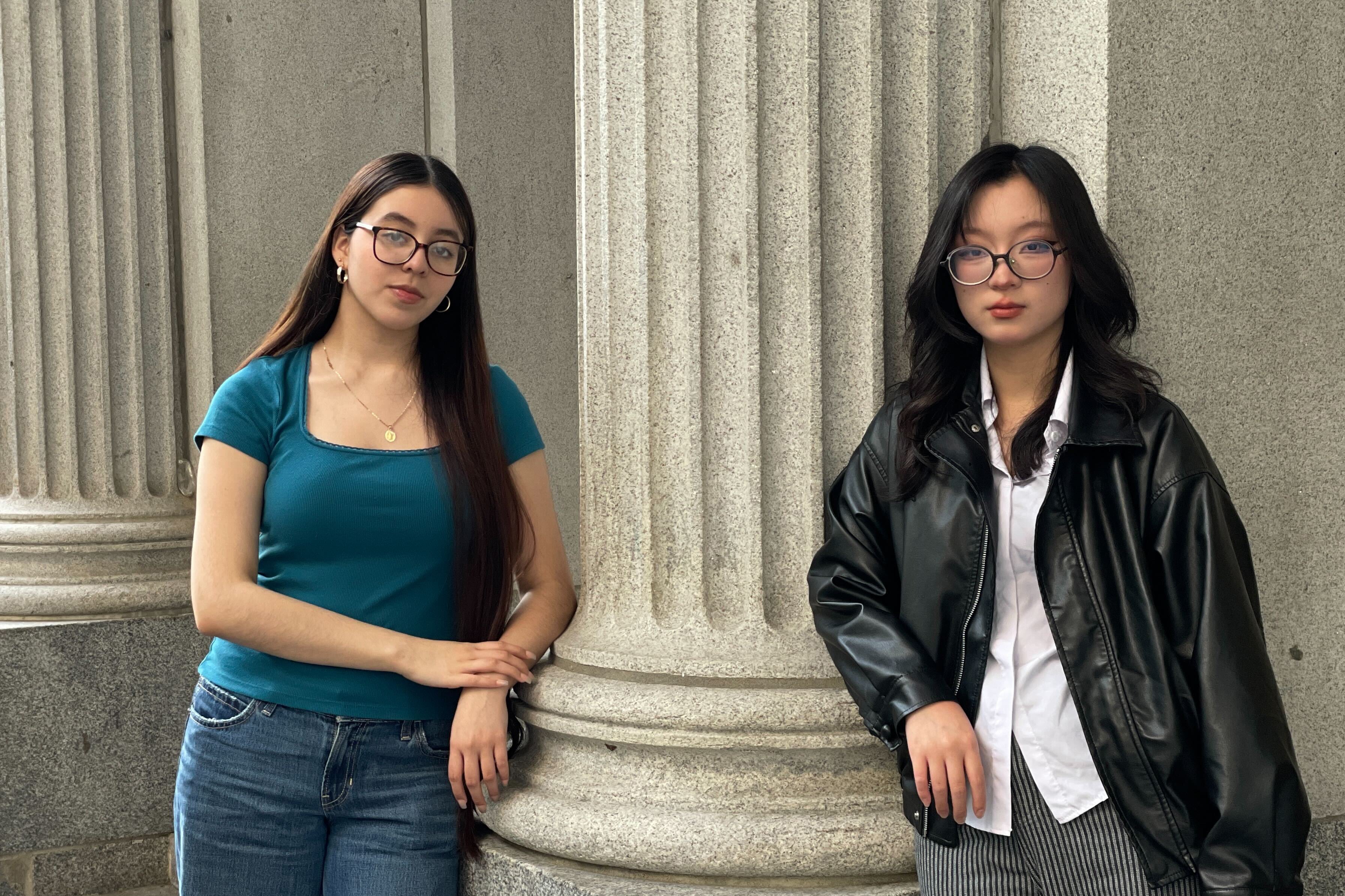 Two high school girls stand next to a stone column while posing for a portrait.