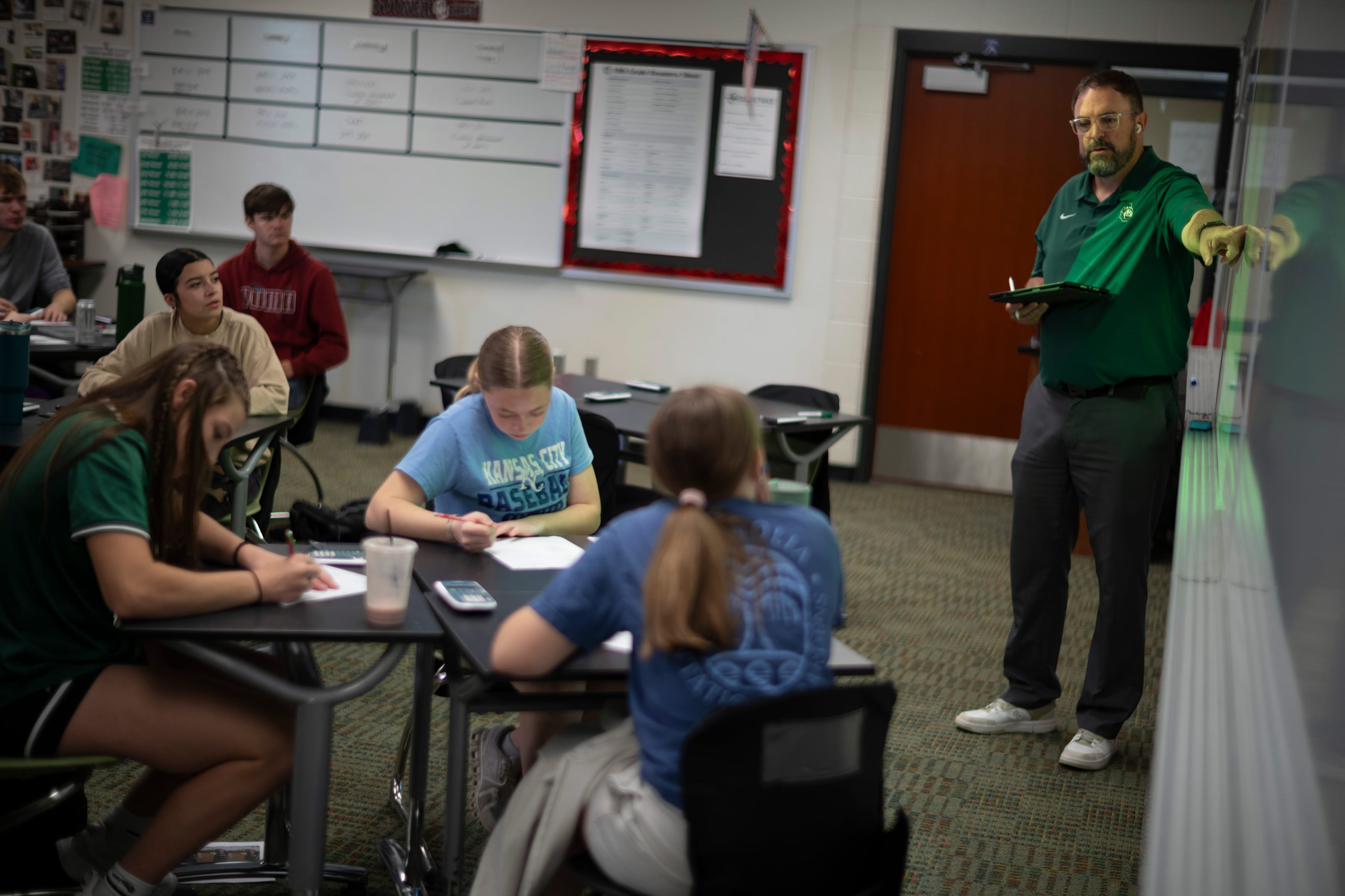 A man in a green shirt points to a white board.