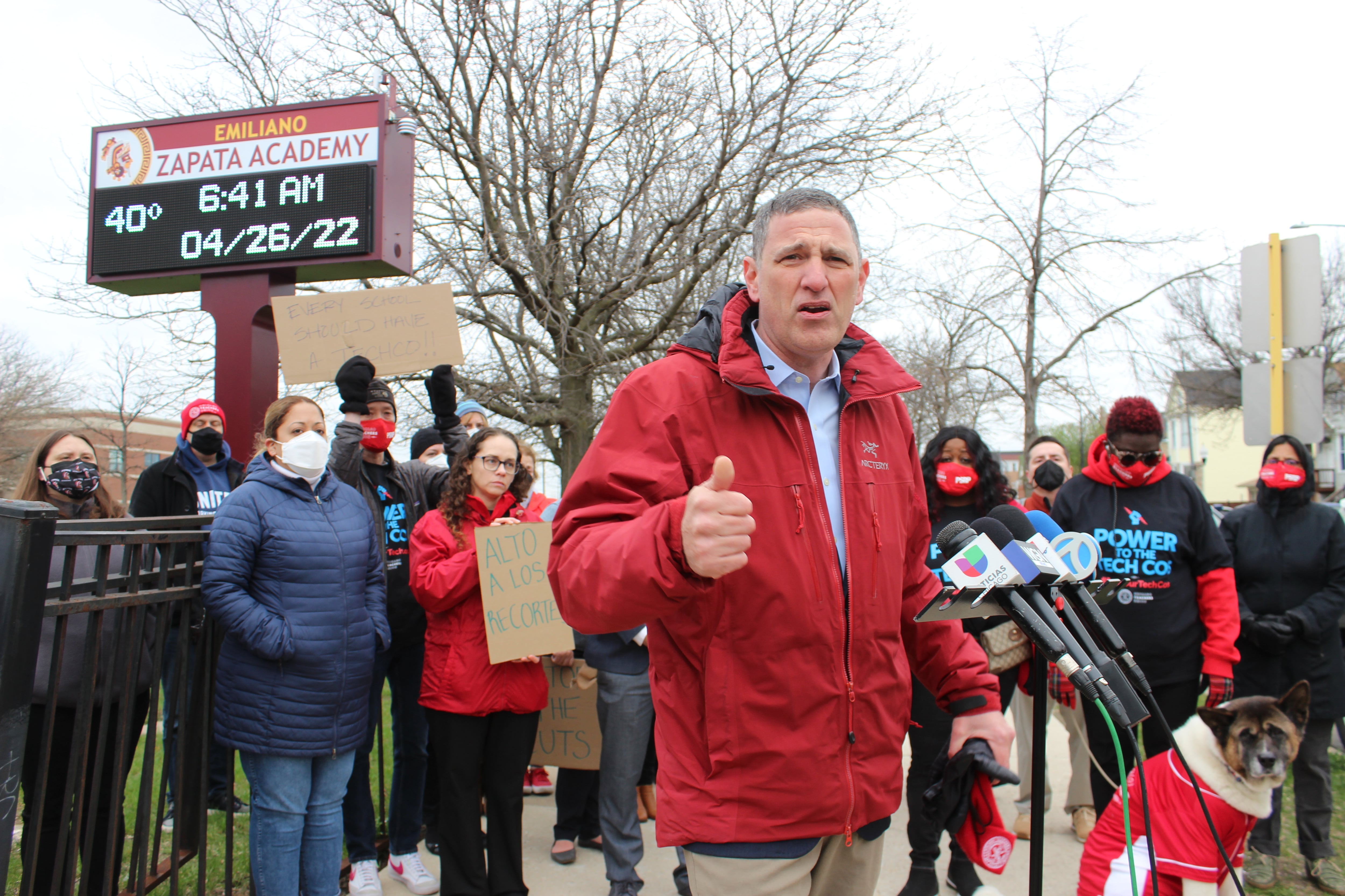 A man wearing red stands in front of a crowd of people outside of an elementary school on Chicago’s Southwest Side.