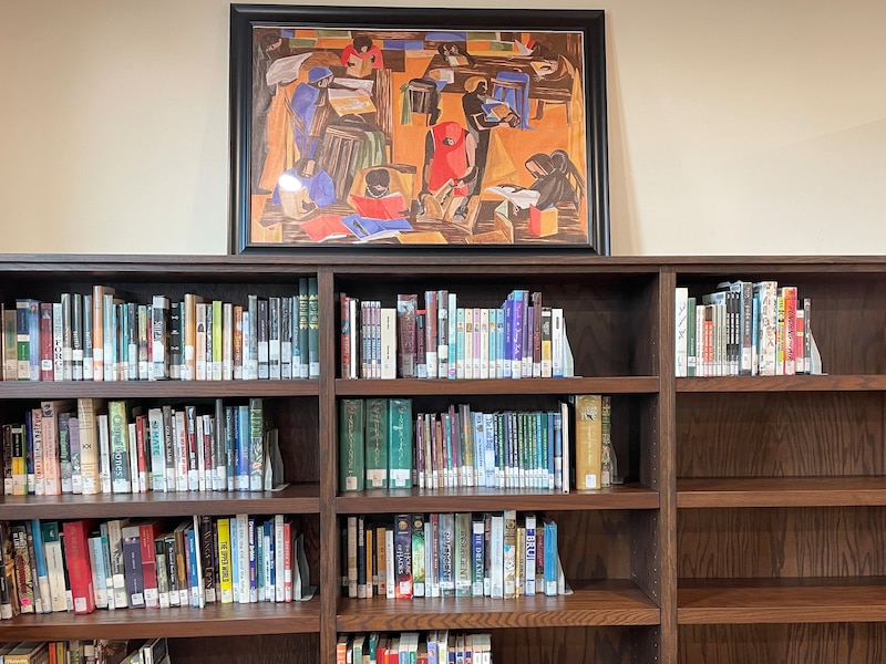 A painting displayed on top of a wooden bookshelf.