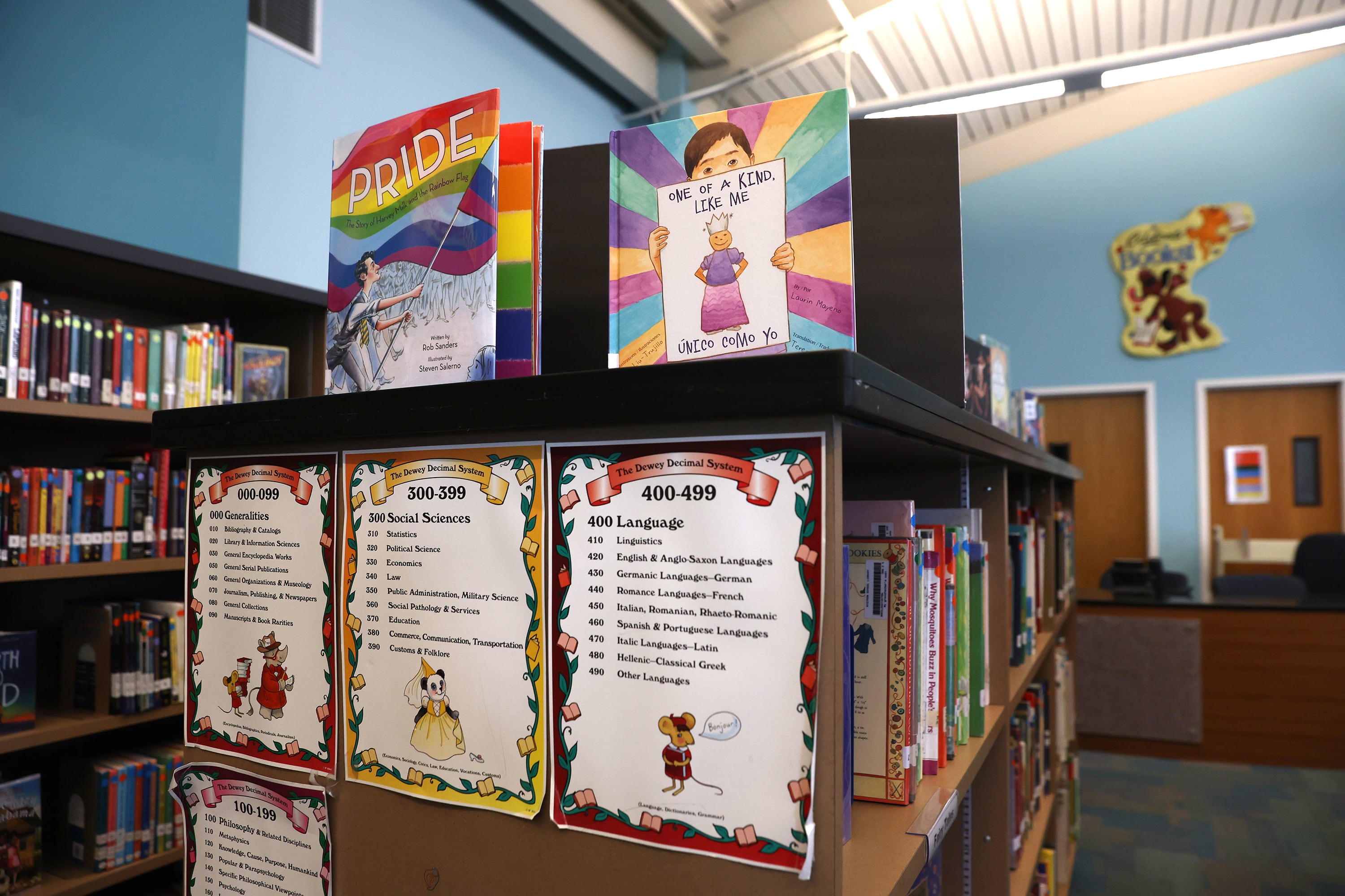 Books and information are stacked on top of and taped to the side of a row of books in a school library.
