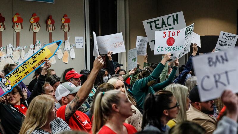 Parents and community members hold up signs on either side of the “CRT” debate at a school board meeting.