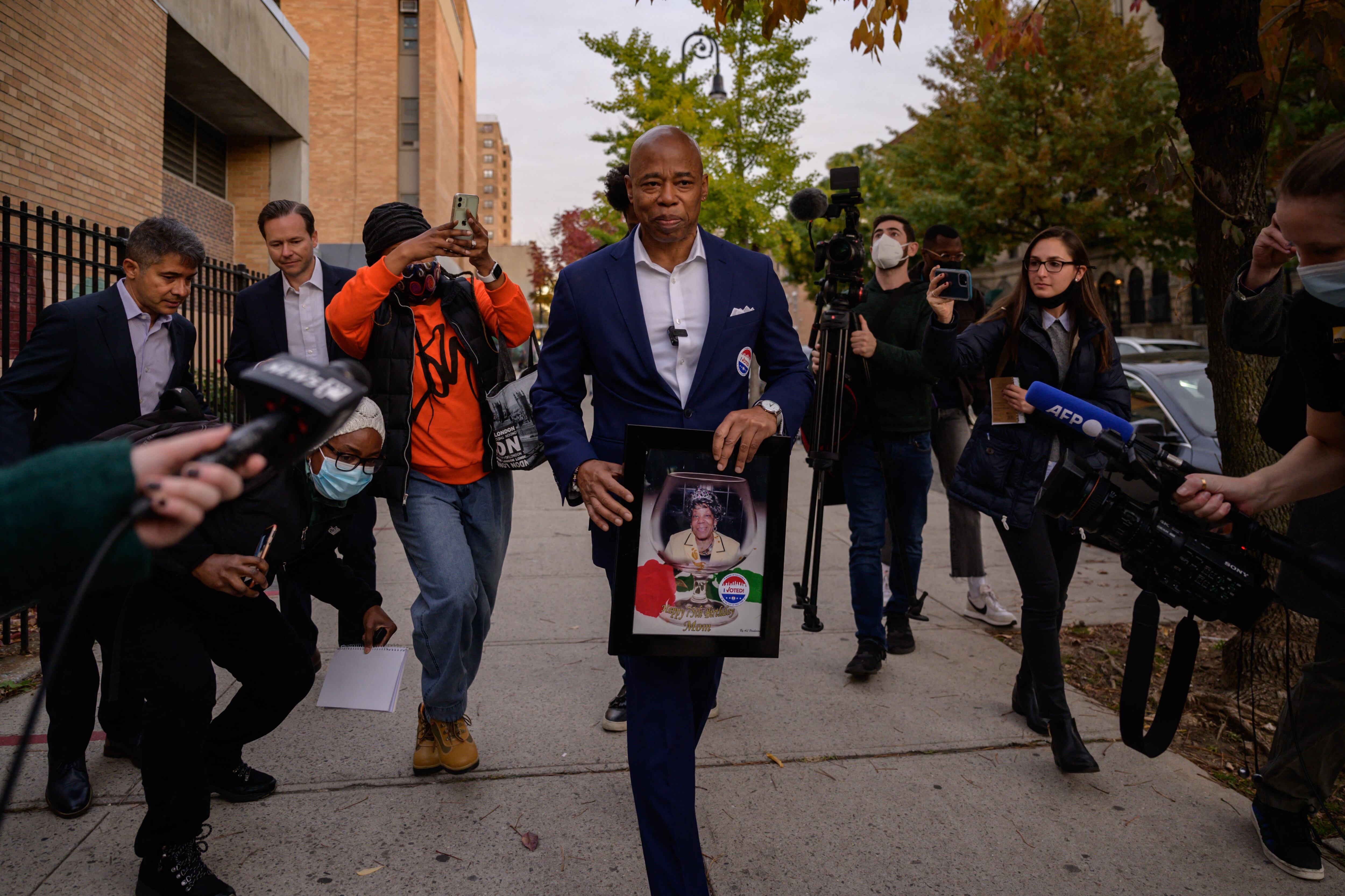 NYC mayoral candidate Eric Adams, the Democratic nominee, leaves his polling place holding a portrait of his mother as members of the media walk alongside him.