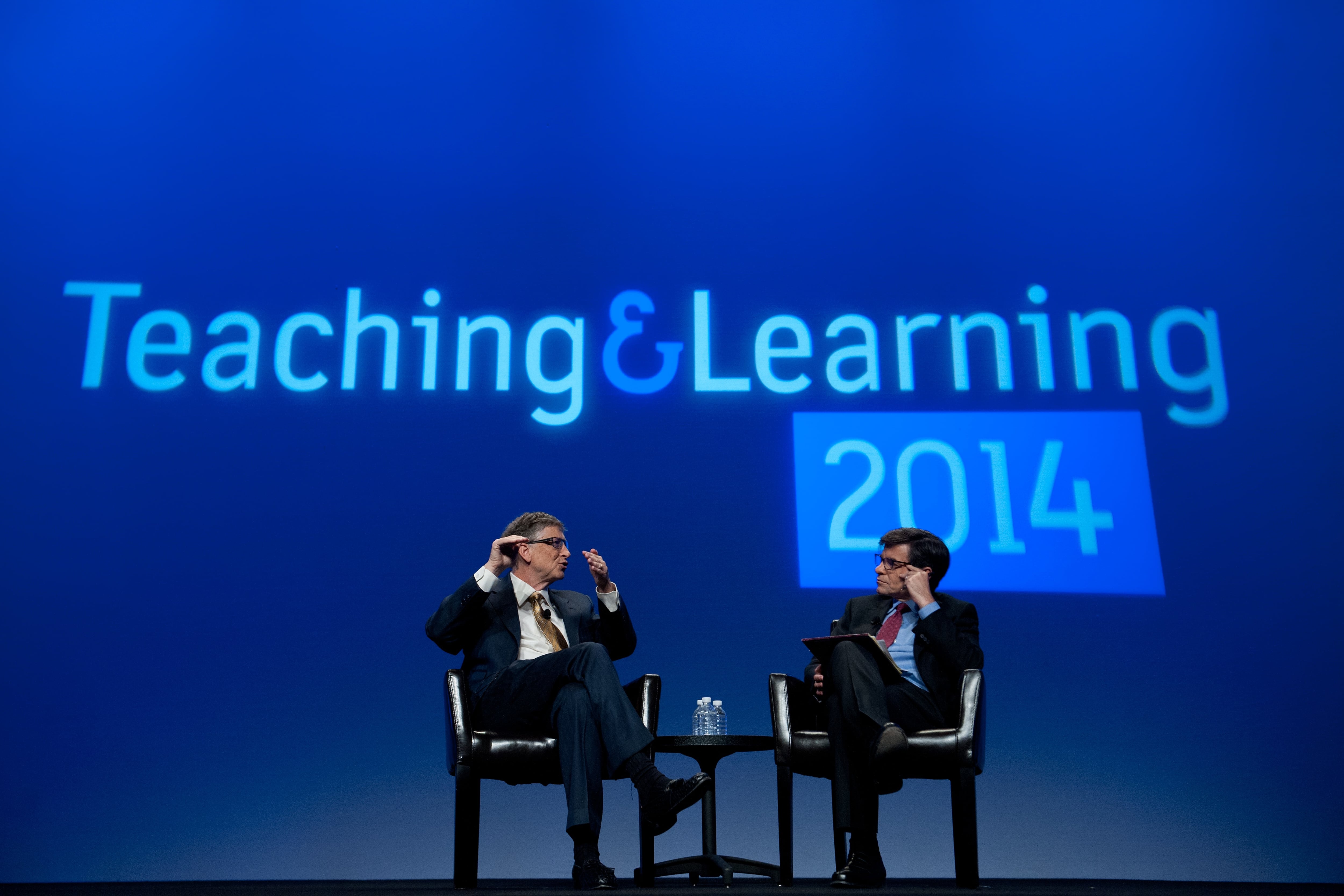 (Left to right) Microsoft founder Bill Gates and television host George Stephanopoulos sit face-to-face on stage during an interview in front of a blue projected backdrop that reads “Teaching & Learning 2014”.