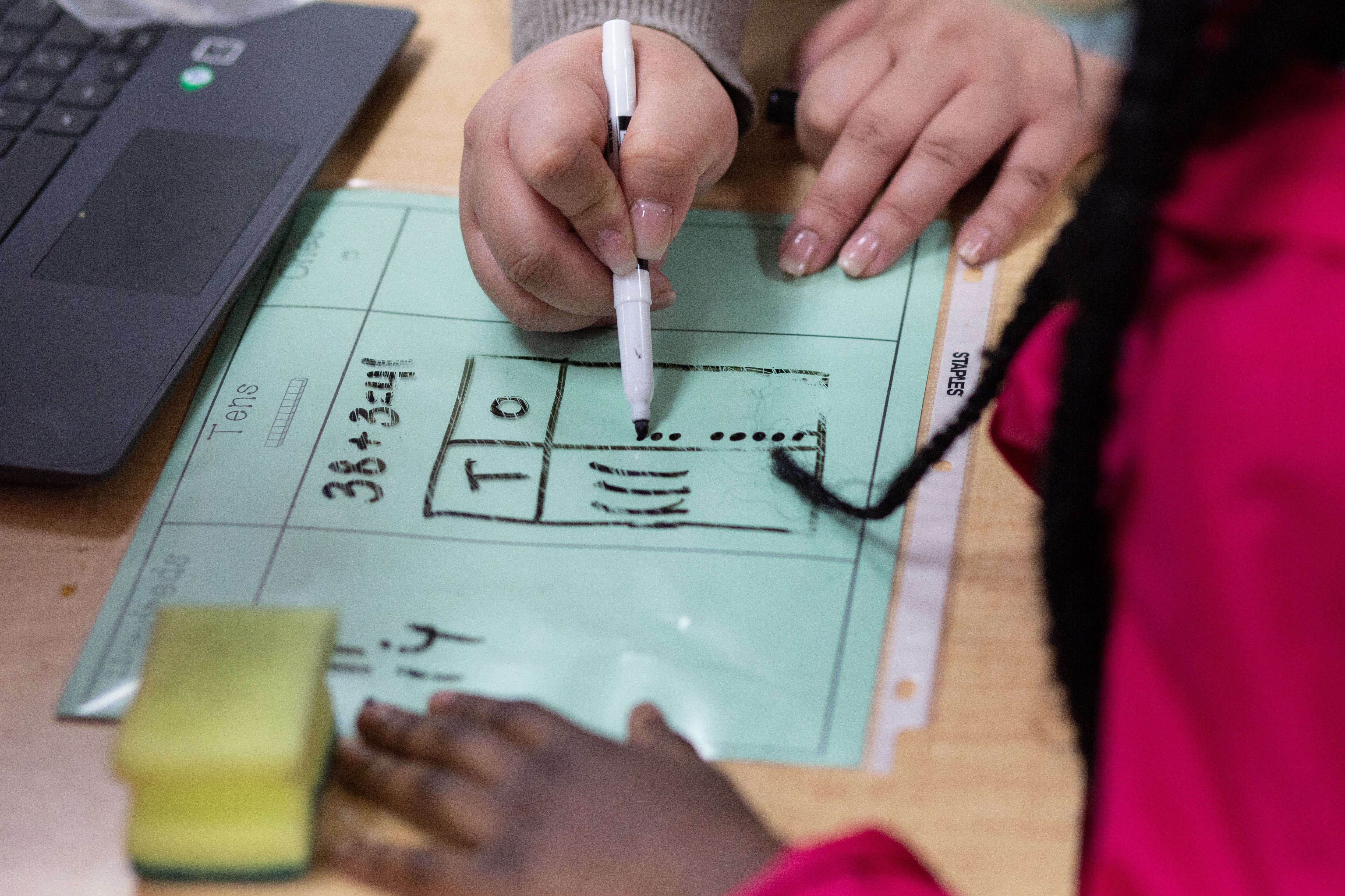 A teacher helps a student wearing a red top with a math problem.