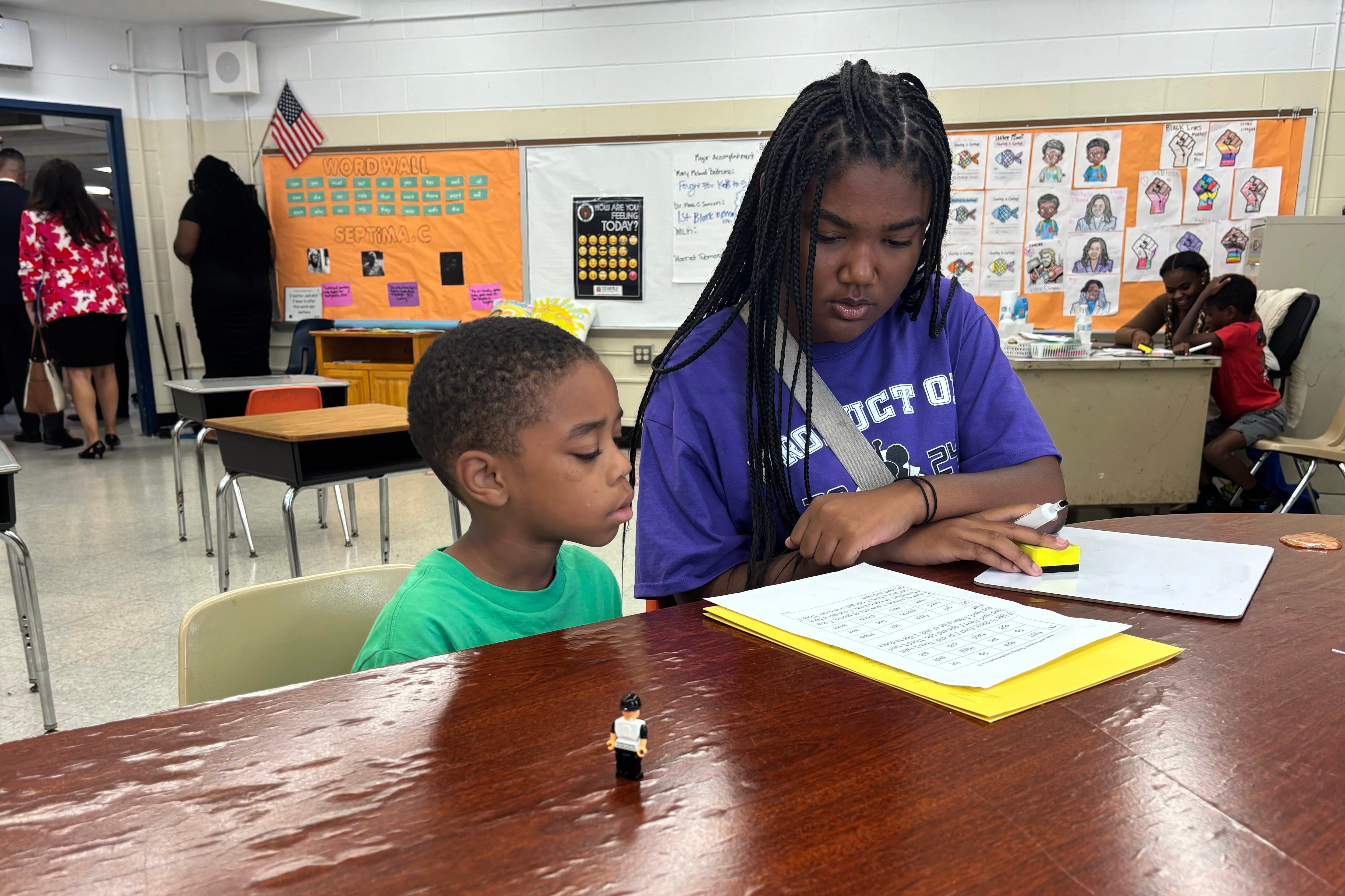 Two students work on a classwork at a table inside a classroom.