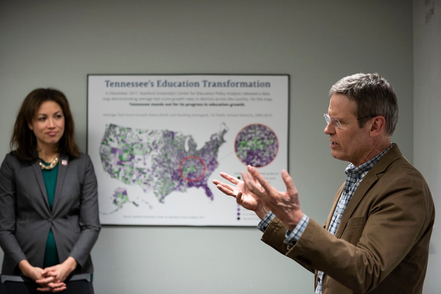 A man gestures while speaking, as a woman looks on in an office setting.