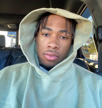 A high school student wearing a grey hoodie poses for a photograph inside of a car.