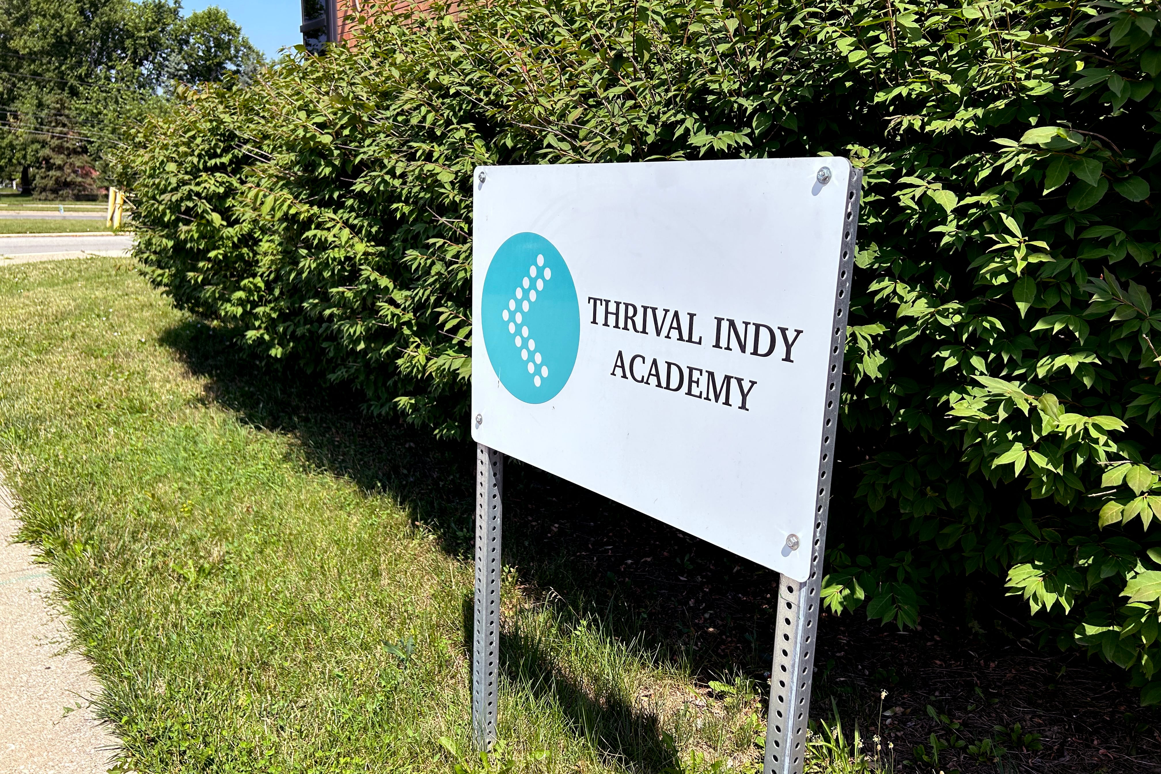 A sign that reads “Thrival Indy Academy” is in grass in front of a bush. 
