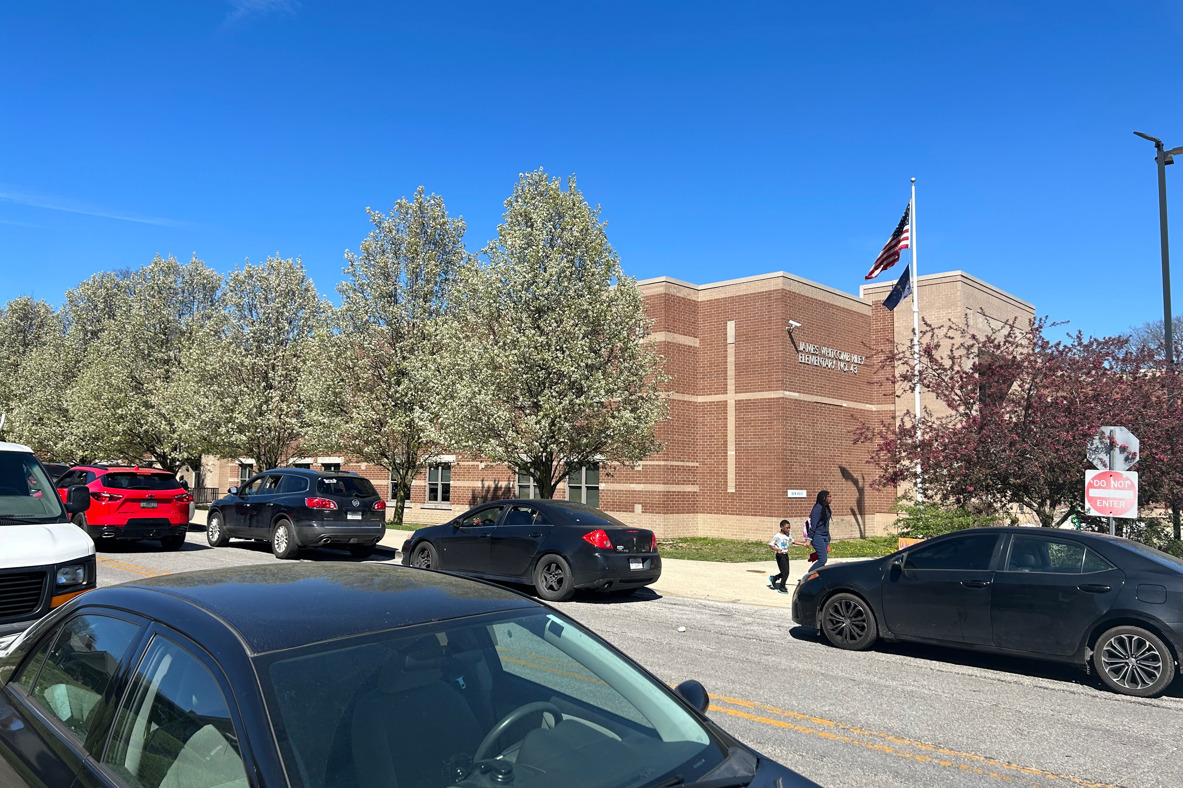 A brick building sits in the background by a road. The building has a sign that reads “James Whitcomb Riley School 43.”