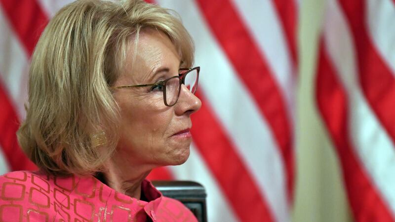 Former U.S. Education Secretary Betsy DeVos is pictured in front of an American flag.