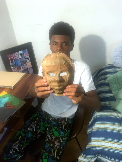 A young boy holds up a handmade mask in his room.