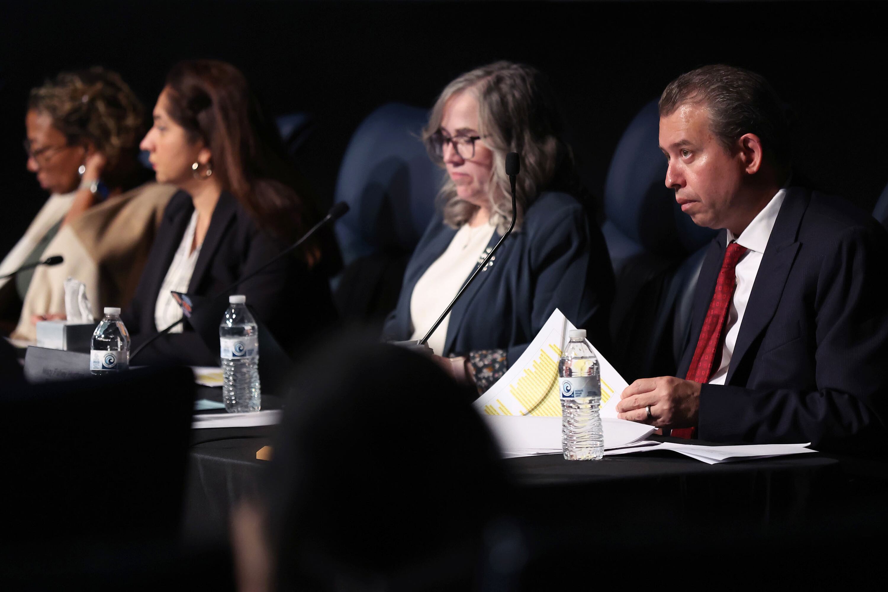 Four adults sit side by side at a long table.