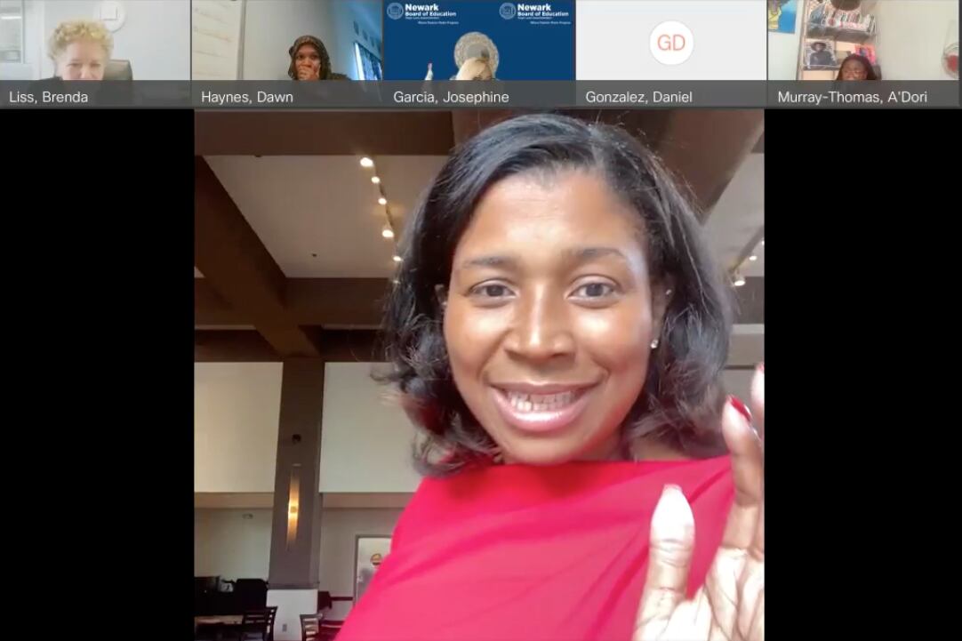 Woman wearing a red top with one hand up looks into the camera as she gets sworn in for school board in a virtual meeting.