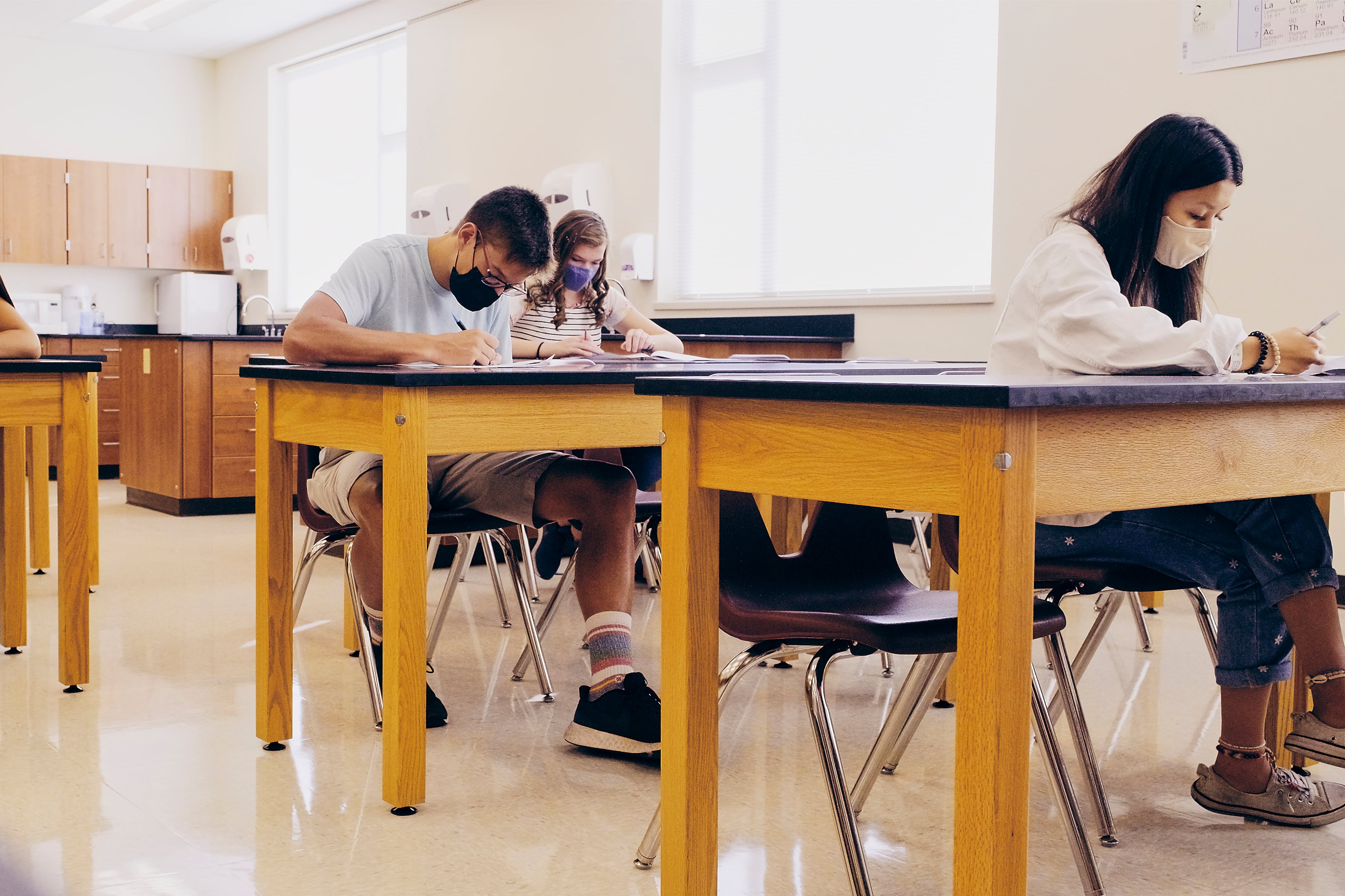 High school students wearing masks sit several feet apart at desks in a classroom,