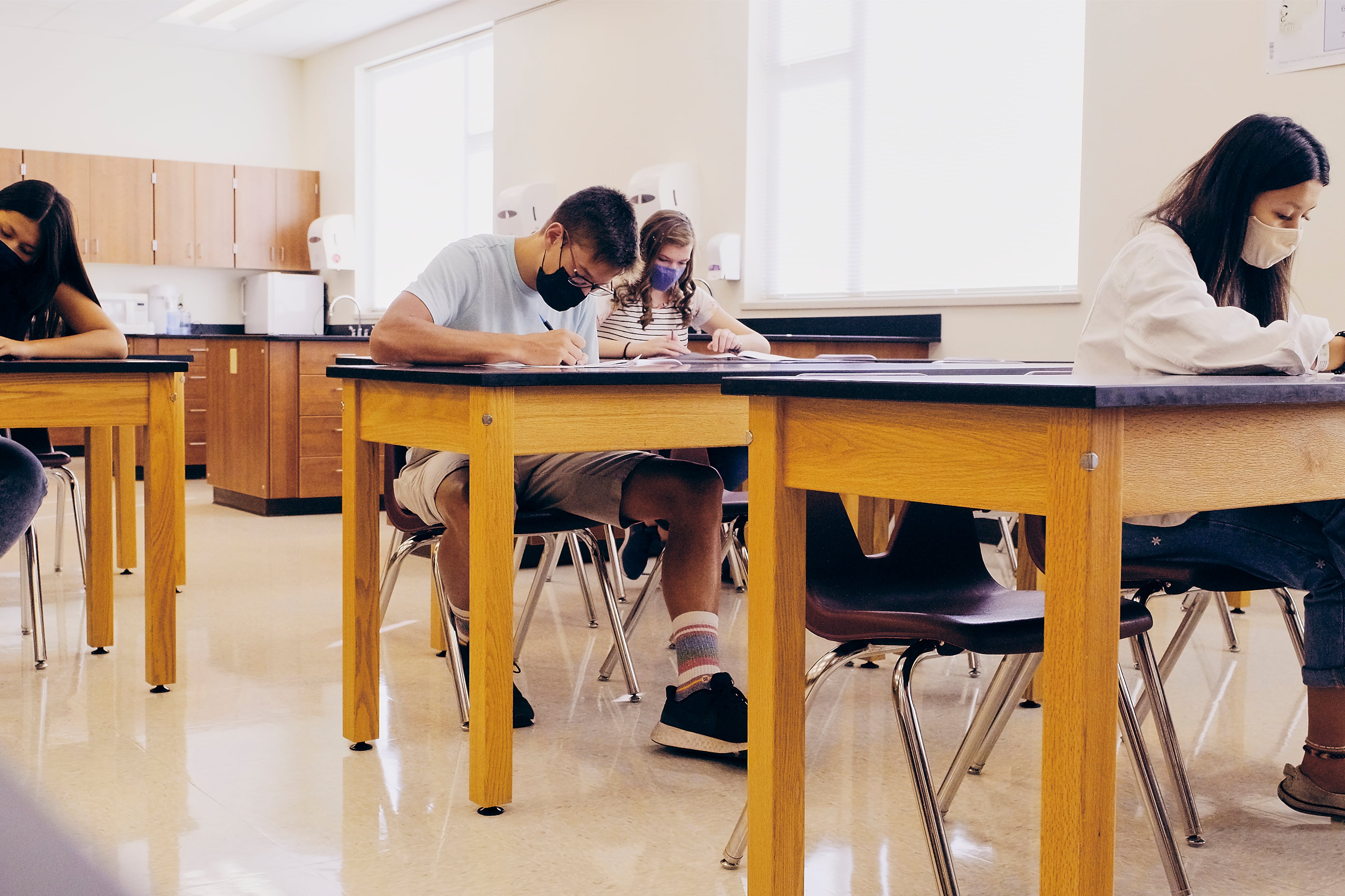 High school students wearing masks sit several feet apart at desks in a classroom,