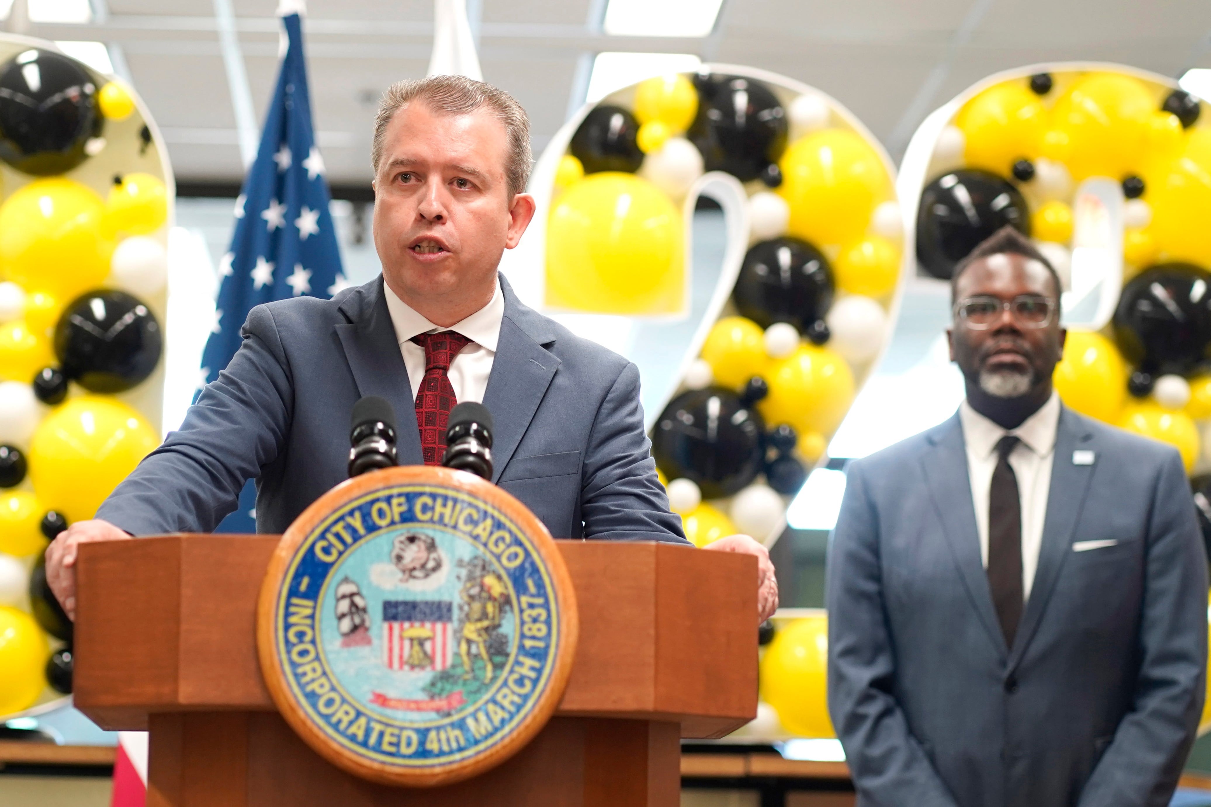 A man in a gray suit jacket stands at a podium
