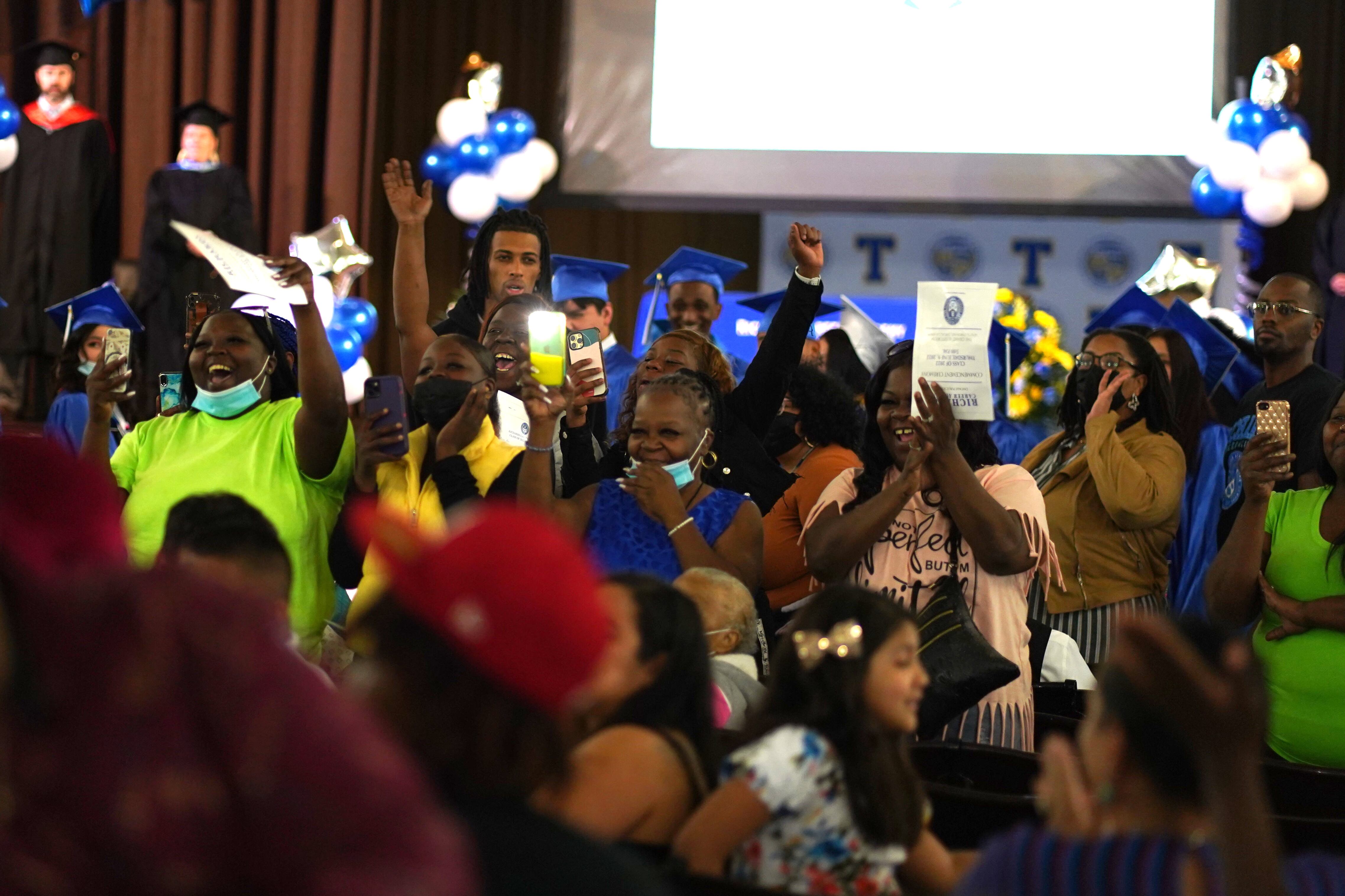 A sea of excited family members cheer on their loved ones from their seats at a graduation ceremony.