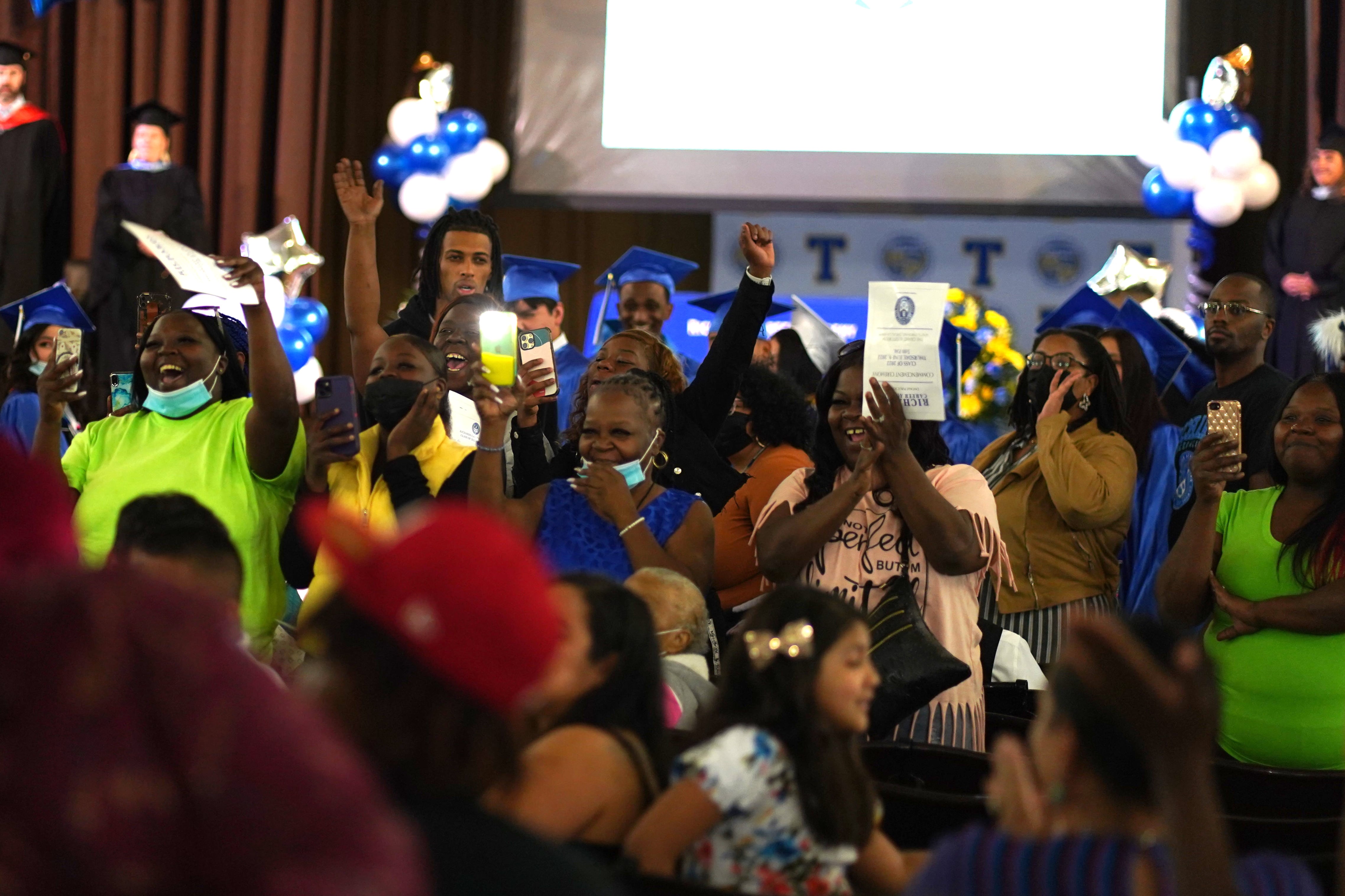 A sea of excited family members cheer on their loved ones from their seats at a graduation ceremony.