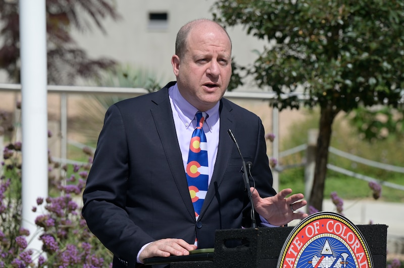 A man in a dark suit jacket speaks at a podium.