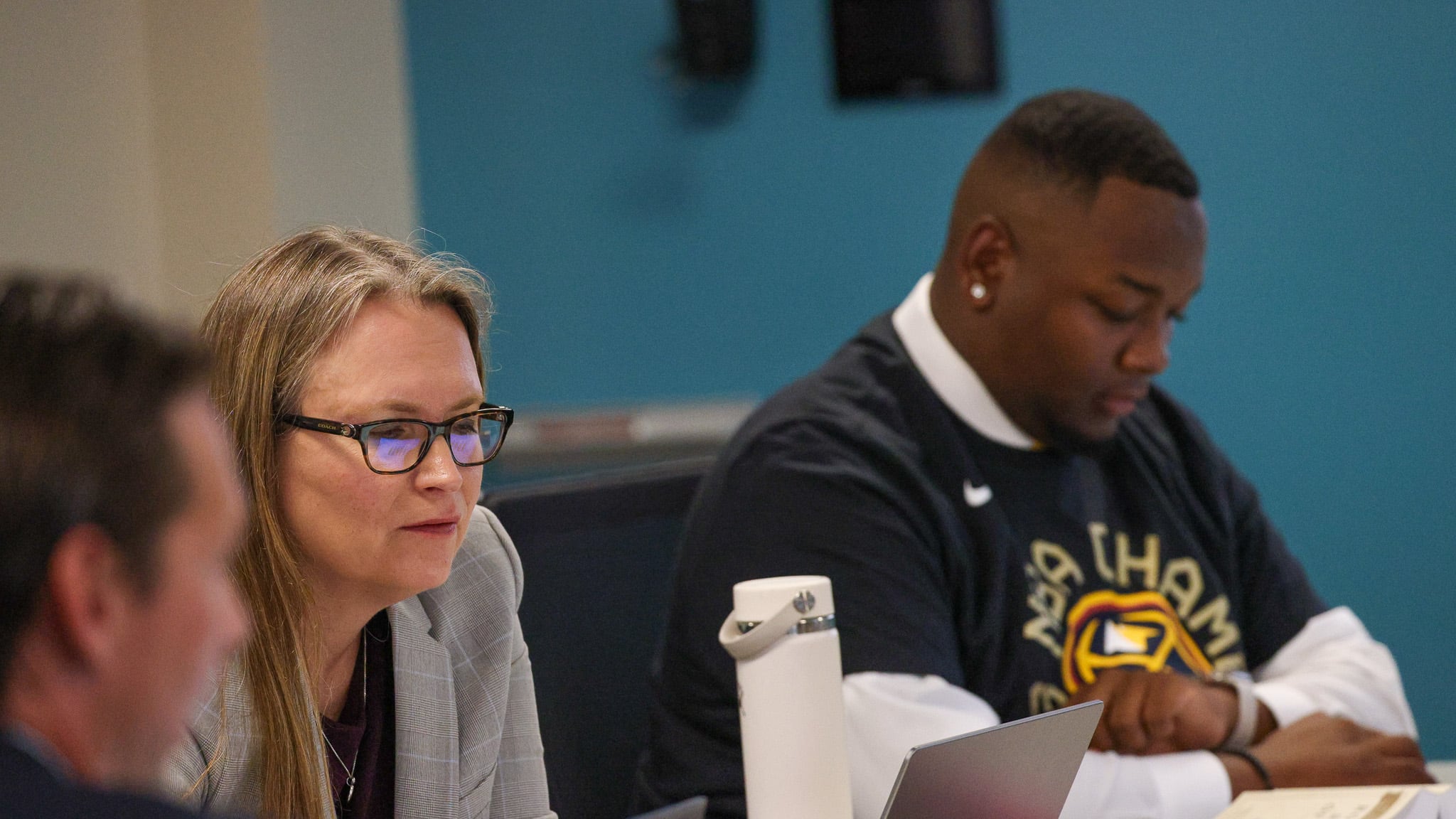 Denver school board members Carrie Olson, center, sits next to member Auon’tai Anderson at a table with laptops on them at school board meeting.