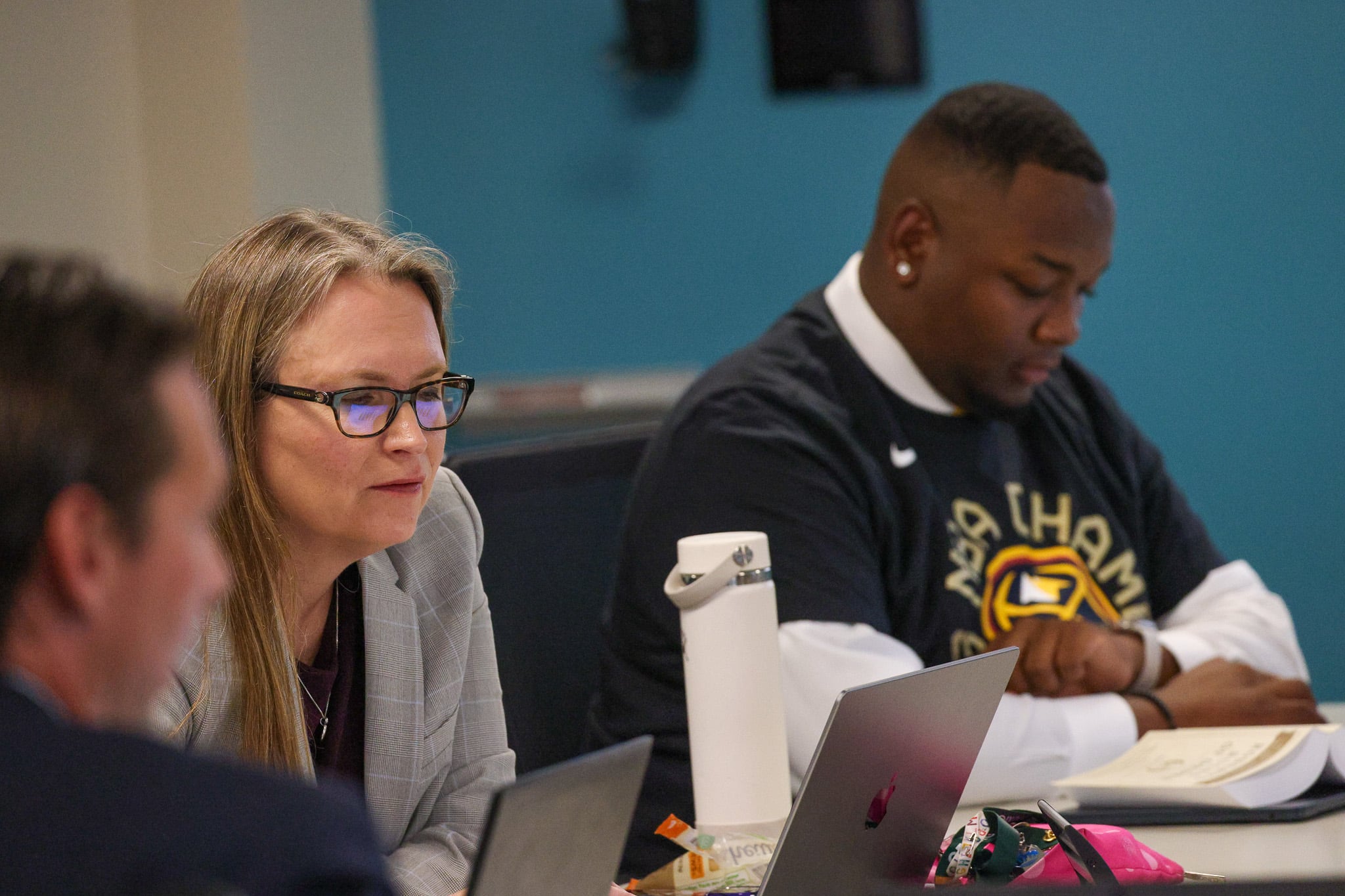 Denver school board members Carrie Olson, center, sits next to member Auon’tai Anderson at a table with laptops on them at school board meeting.