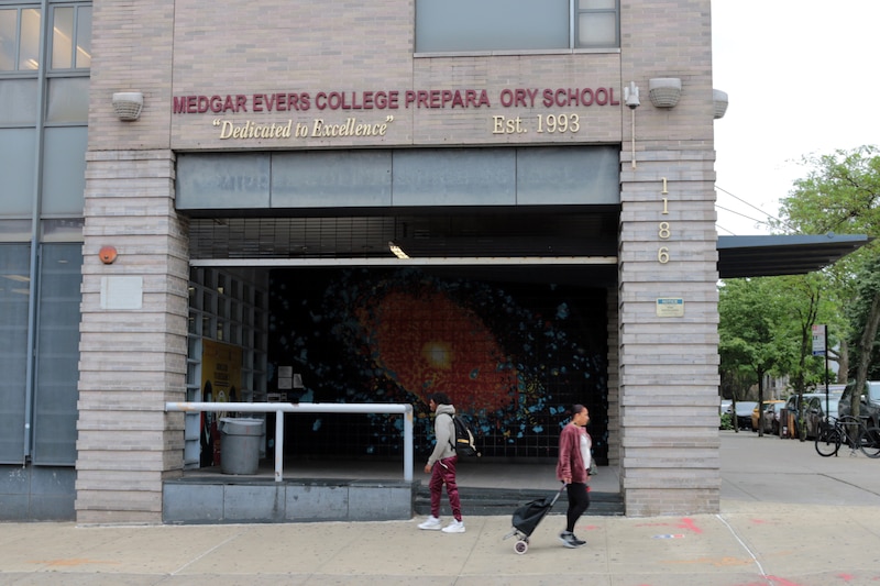 The entrance to a high school while two people cross in front of the building.