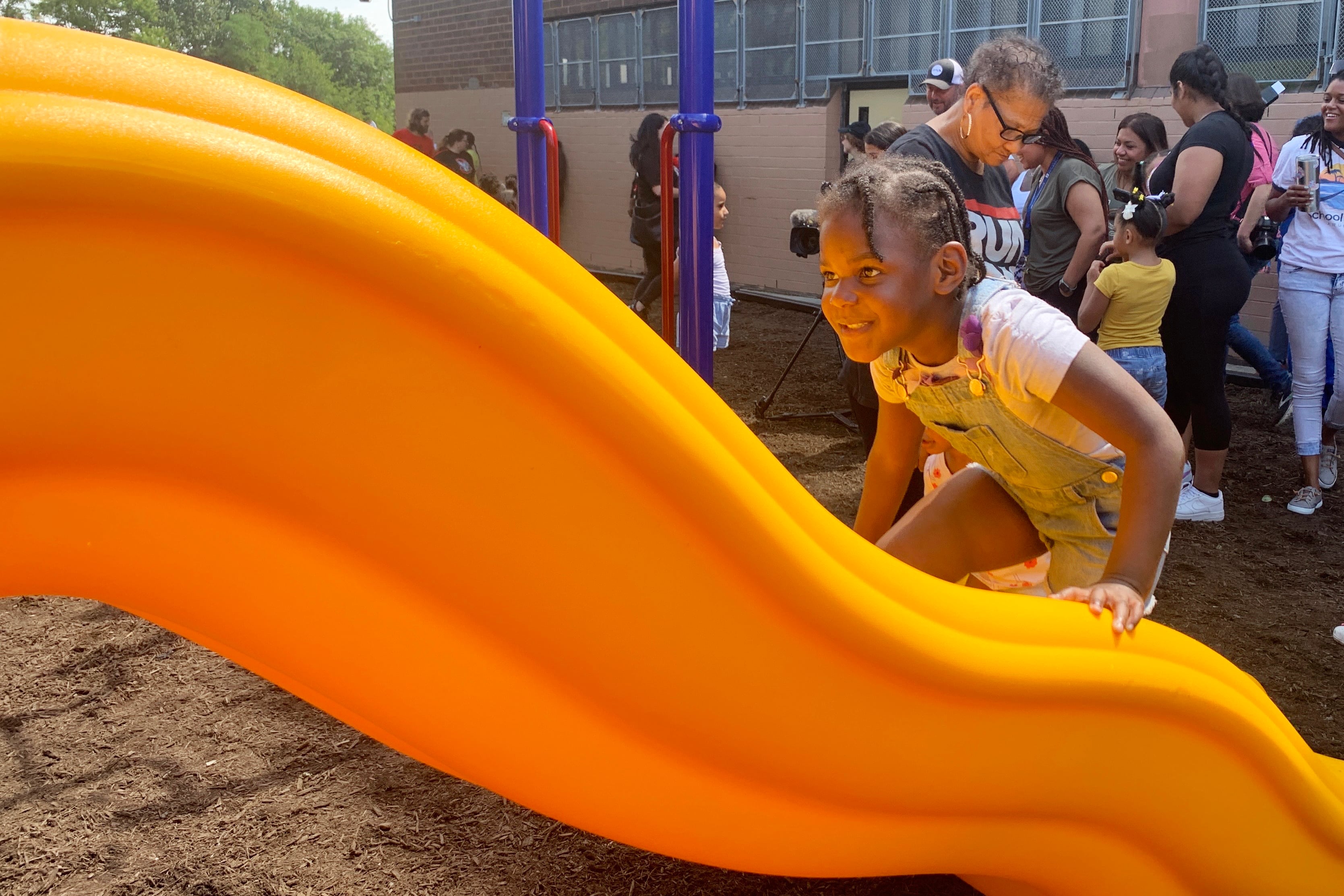 a girl in shorts overalls and a white t-shirt climbs up a bright yellow slide