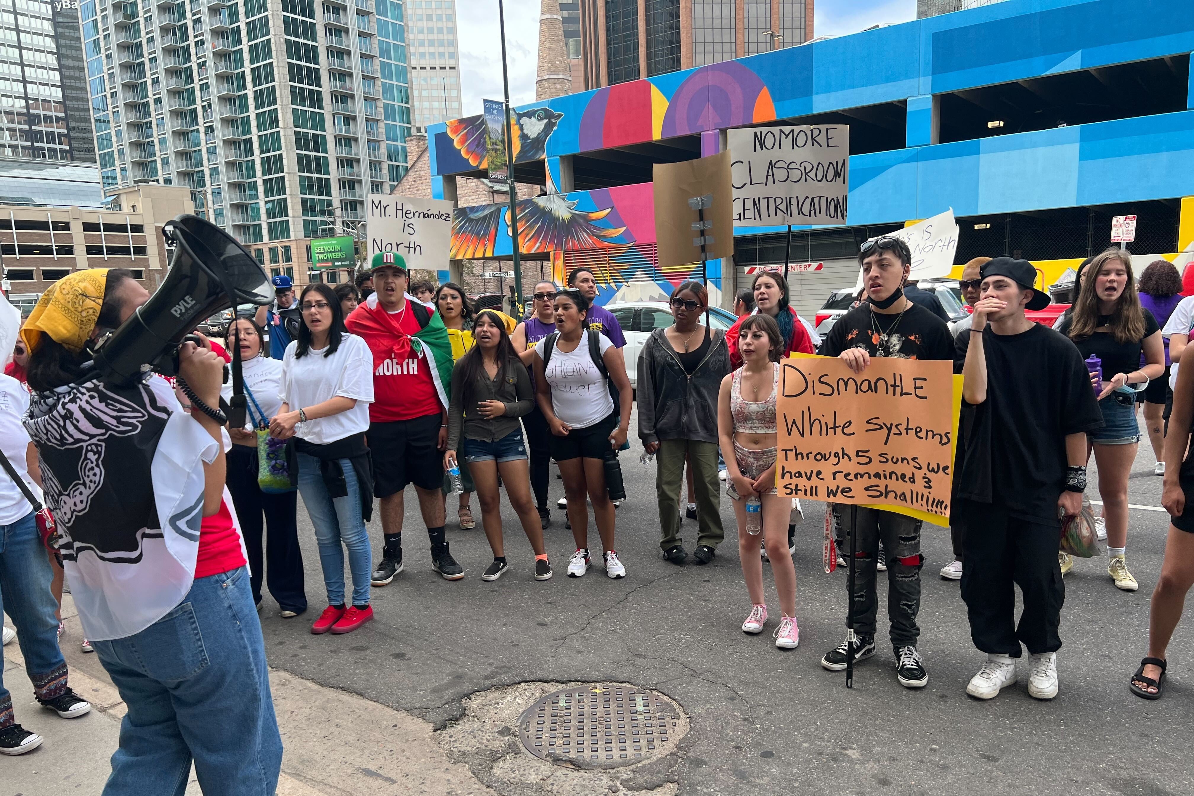A group of high school students hold signs as they protest in the middle of a downtown Denver street.