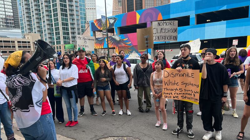 A group of high school students hold signs as they protest in the middle of a downtown Denver street.