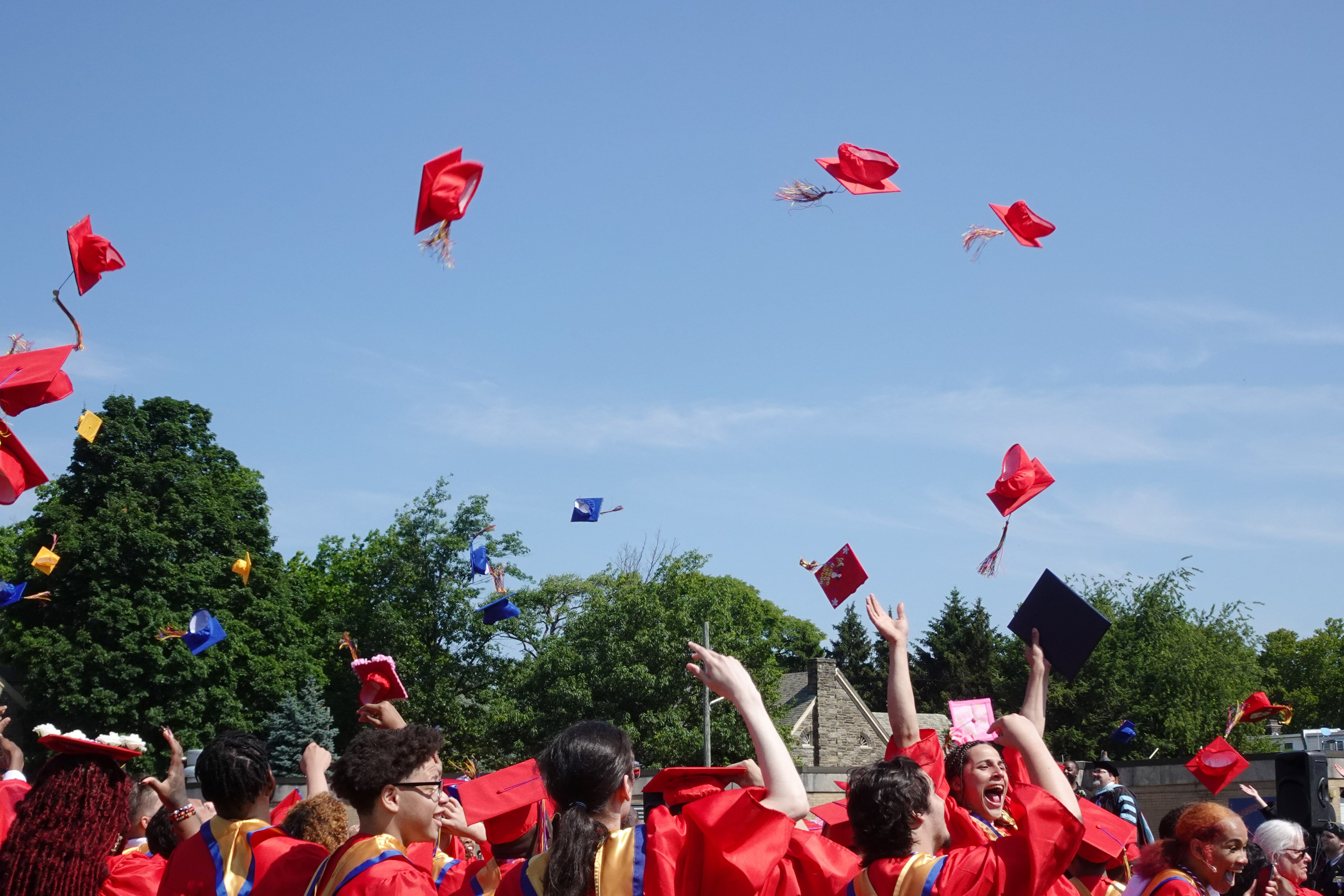 High school graduates toss their red graduation caps into the air with a blue sky in the background.