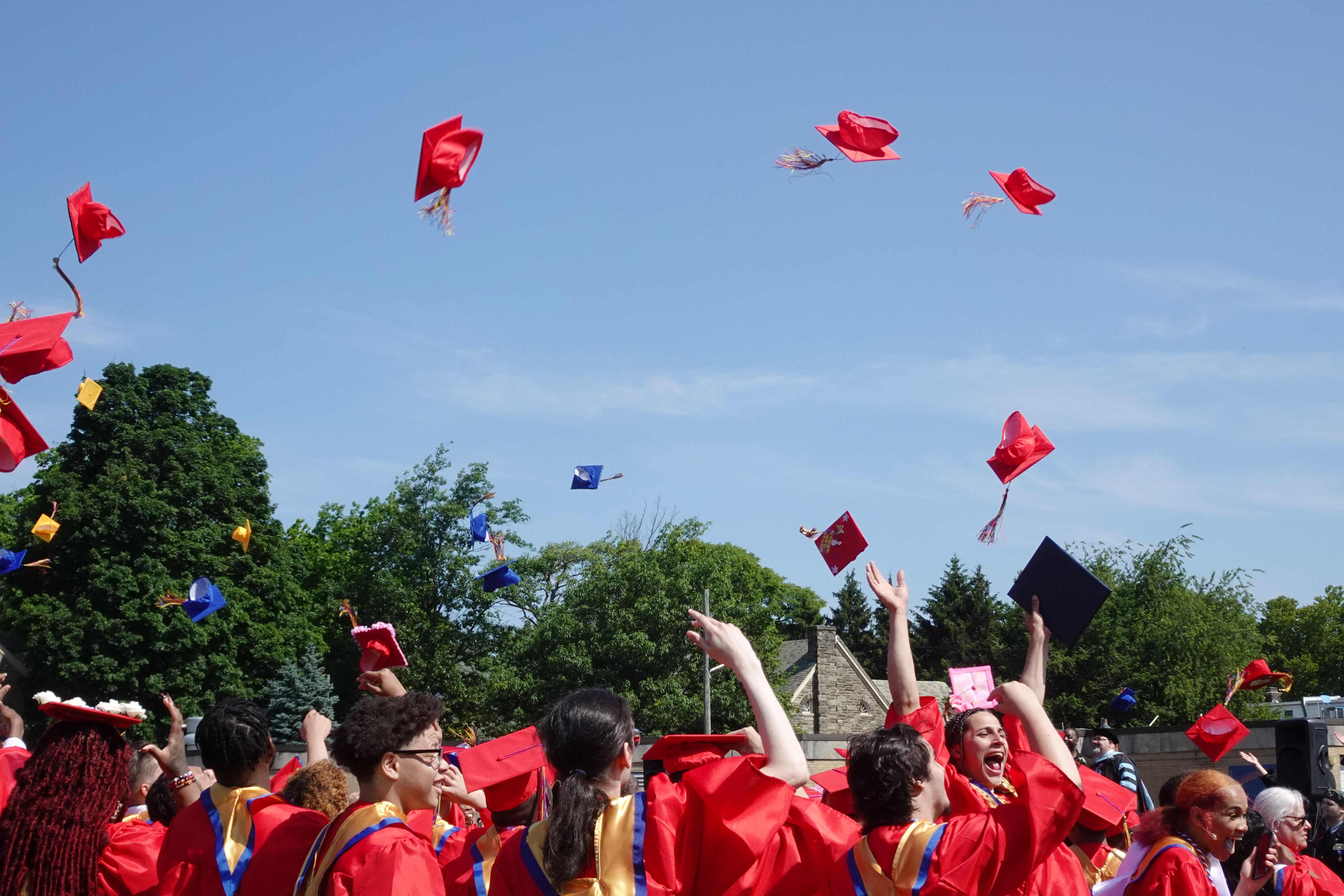 High school graduates toss their red graduation caps into the air with a blue sky in the background.
