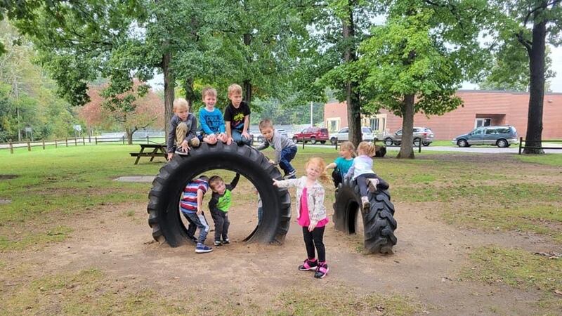 Young children play around two large playground tires embedded in a grassy space during programming at Wawasee Community School Corporation’s early learning program.