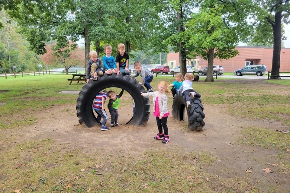 Young children play around two large playground tires embedded in a grassy space during programming at Wawasee Community School Corporation’s early learning program.