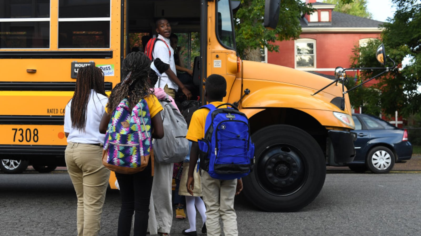 A group of students with their backs to the camera board a yellow school bus.