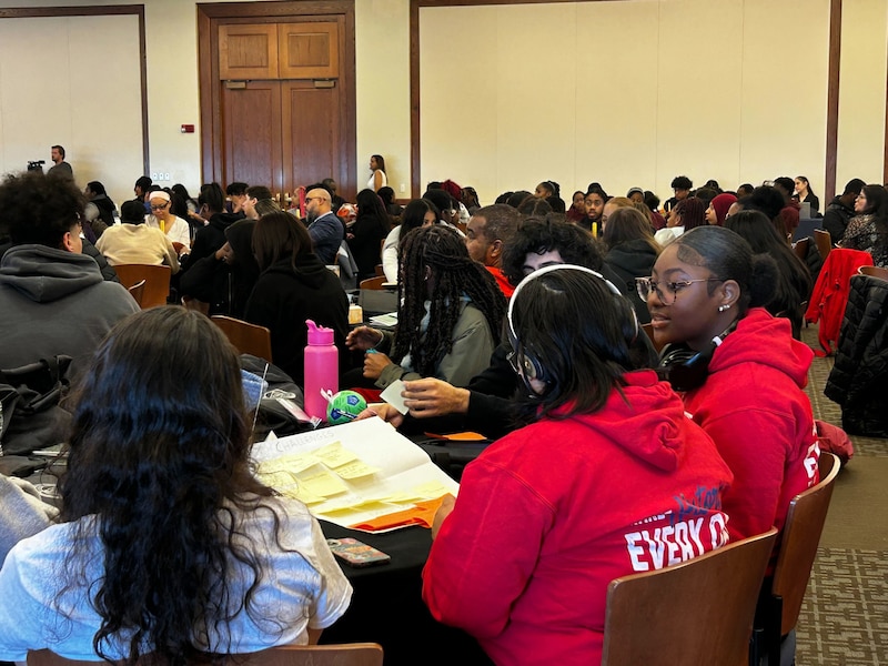 A large room of adults and students in a conference room.