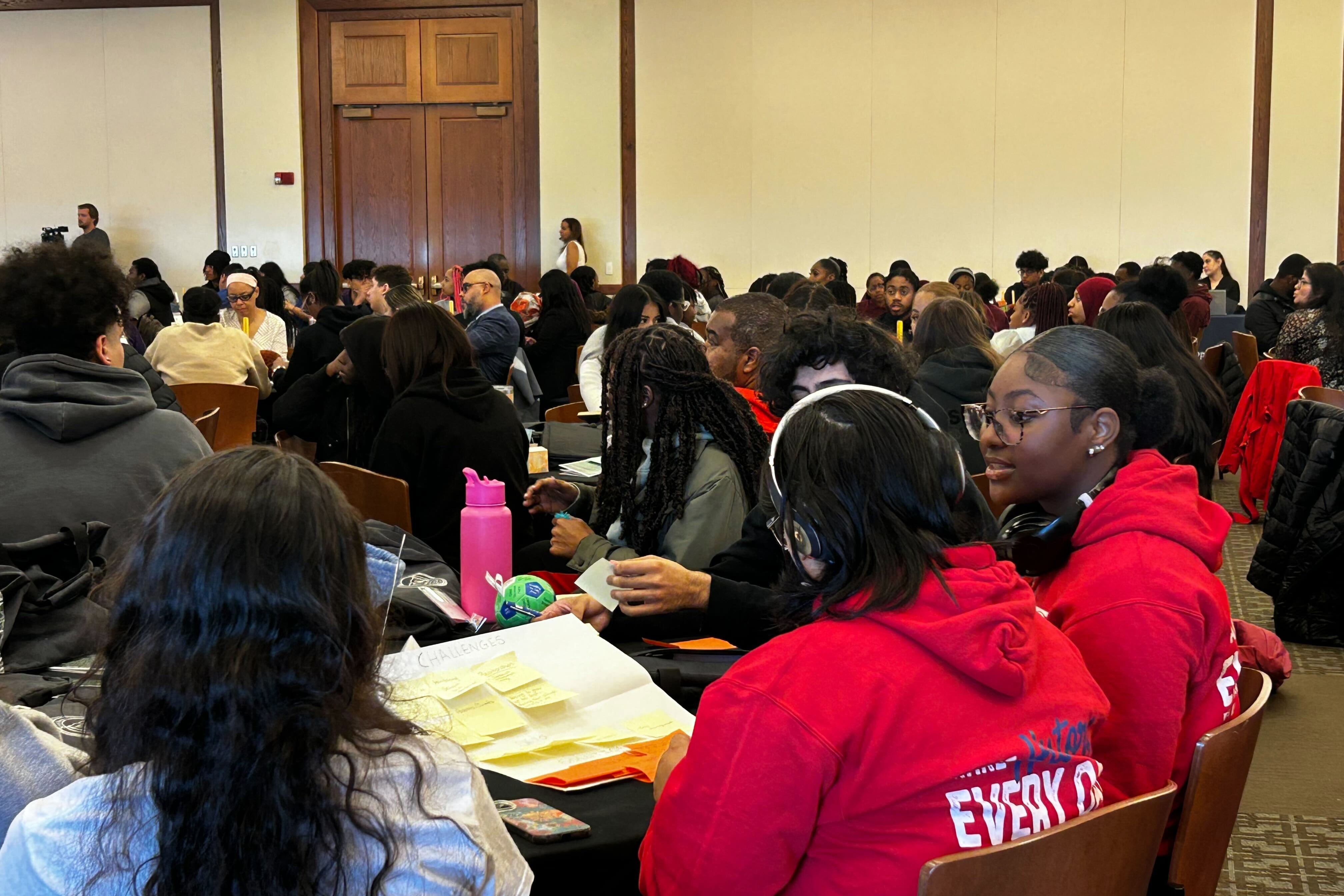 A large room of adults and students in a conference room.