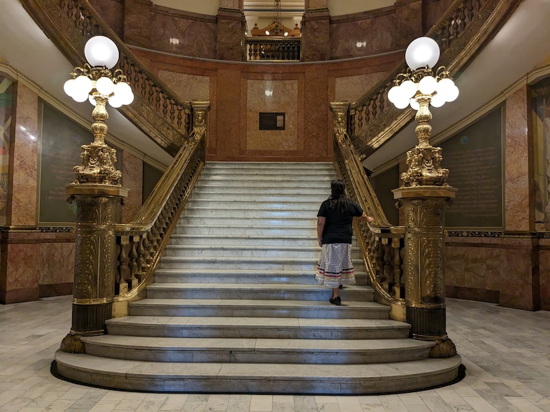 A person walks up a large staircase with two large lights at each post at the bottom of stairs.