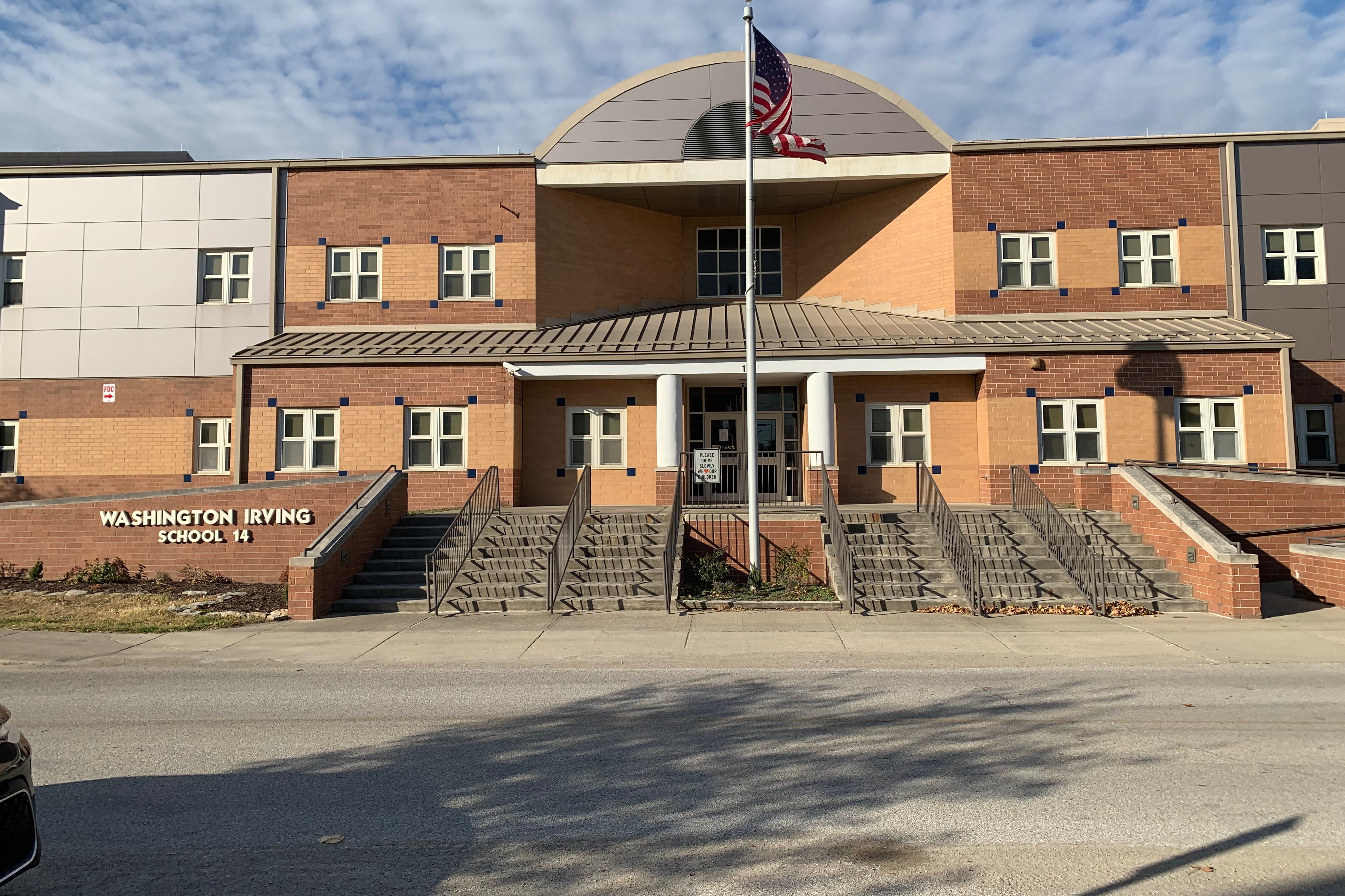 A brick building with an American flag sits behind a set of stairs. On the left of the stairs are white letters that read “Washington Irving School 14.”