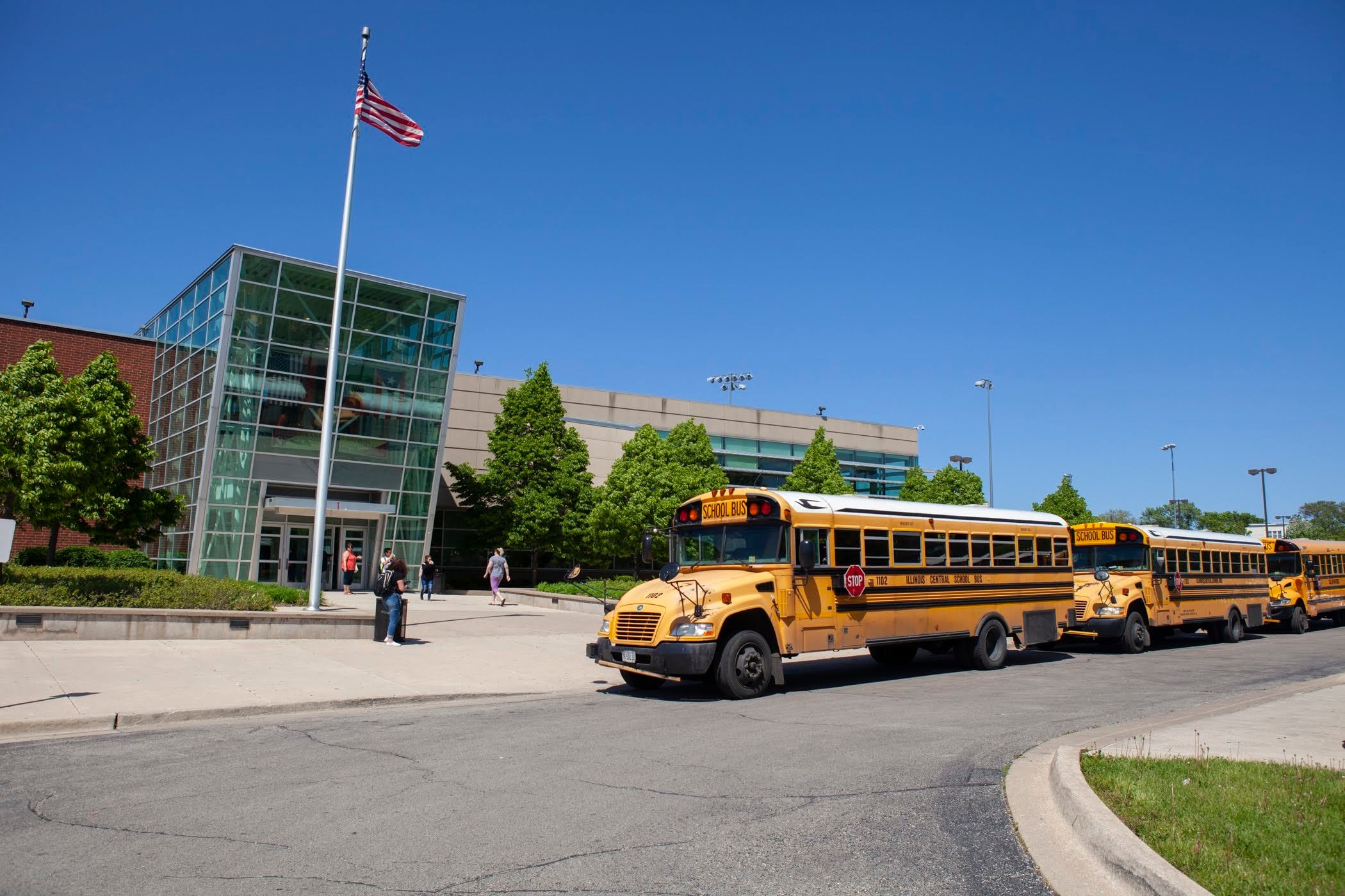School buses and an American flag are at the front of North-Grand High School in Chicago, with school buses lined up in front of the campus.