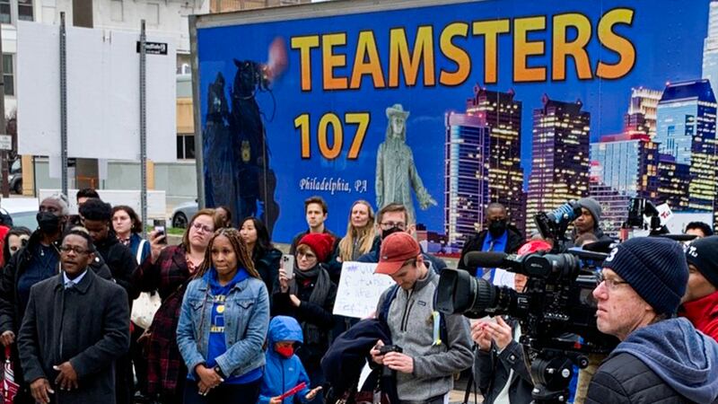 A crowd of people in front of school district headquarters in Philadelphia with a Teamsters truck in the background